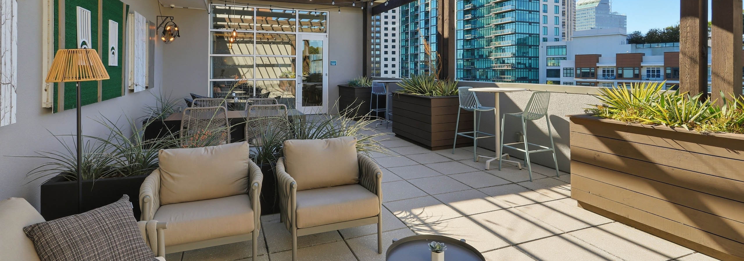 Exterior view of a rooftop lounge at AMLI Buckhead with couches and chairs and side tables with planter boxes and blue sky