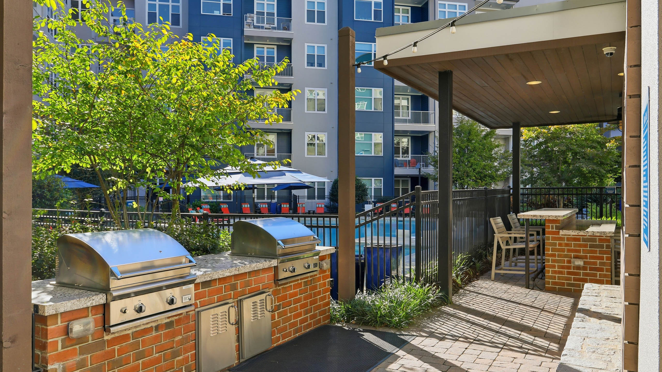An exterior view of a BBQ grilling area at AMLI Buckhead with two stainless steel covered grills on top of marble counters