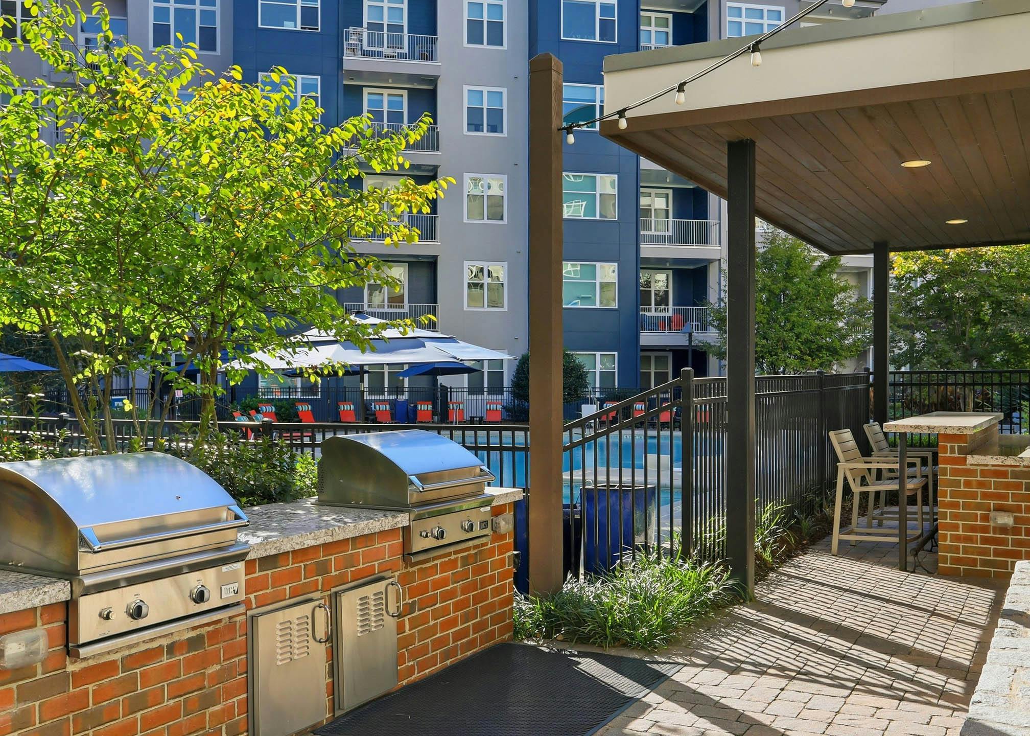 An exterior view of a BBQ grilling area at AMLI Buckhead with two stainless steel covered grills on top of marble counters