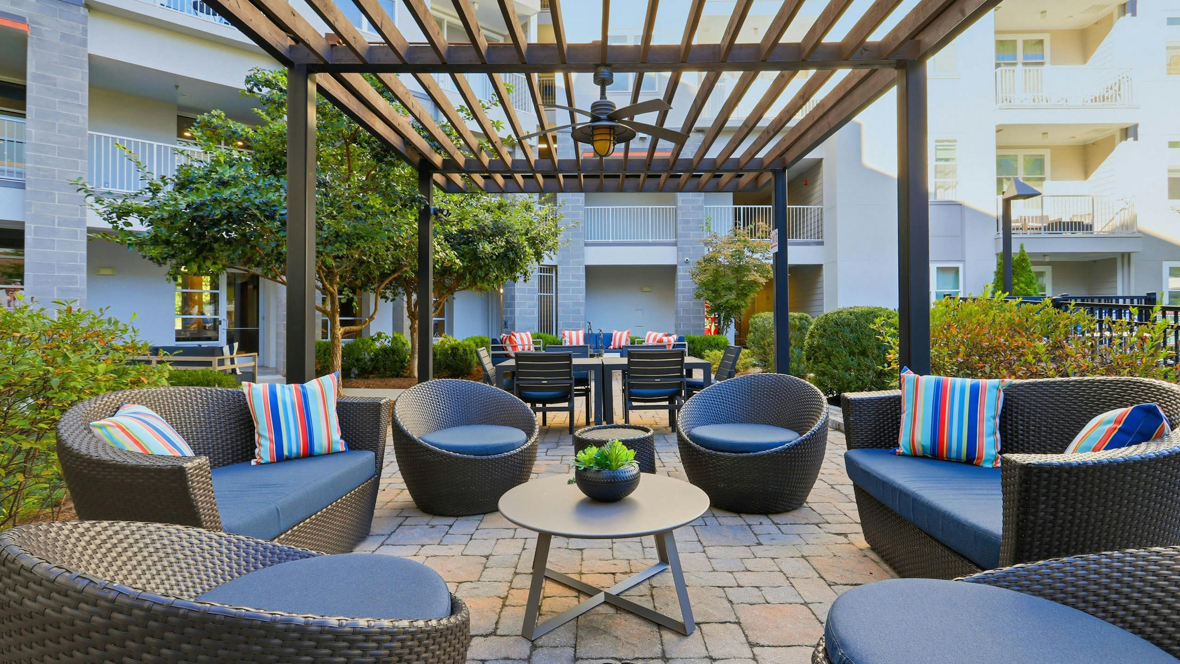 Outdoor resident lounge amenity area at AMLI Buckhead apartments with chairs and cushions and an overhead wooden trellis