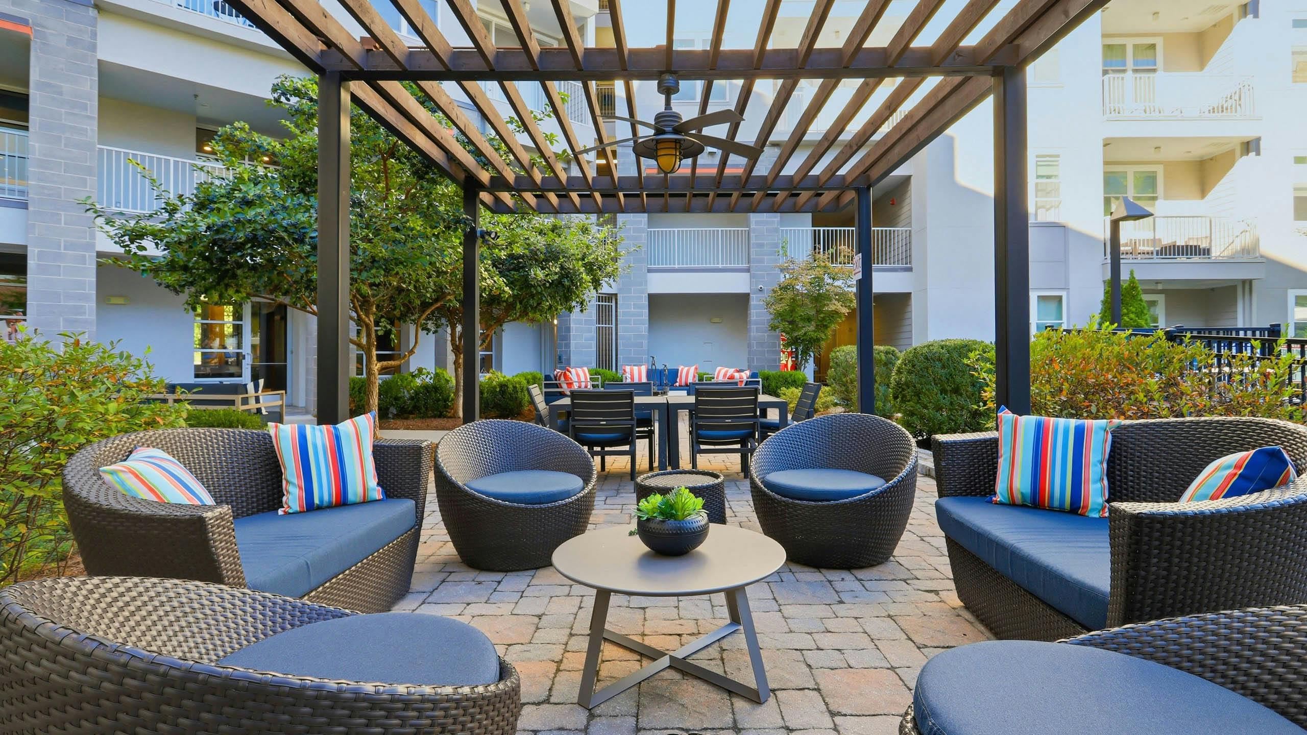Outdoor resident lounge amenity area at AMLI Buckhead apartments with chairs and cushions and an overhead wooden trellis