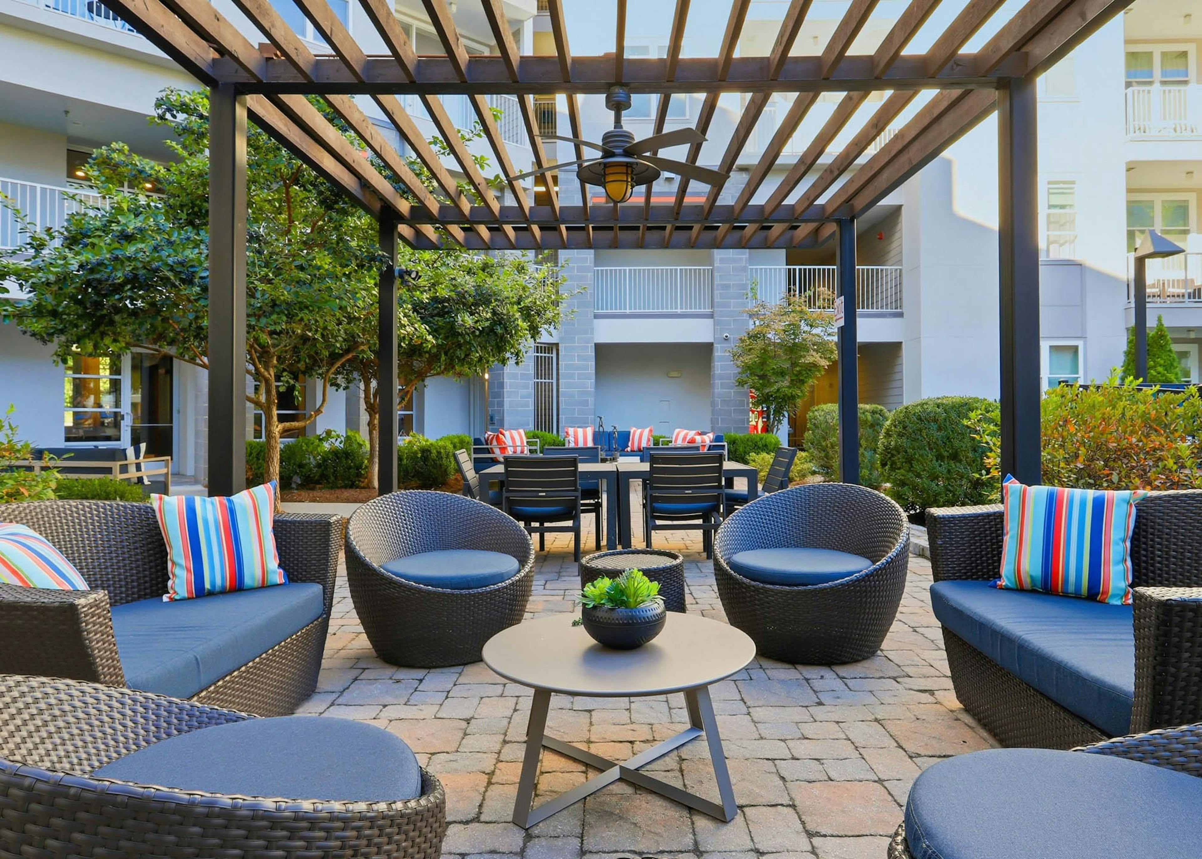 Outdoor resident lounge amenity area at AMLI Buckhead apartments with chairs and cushions and an overhead wooden trellis