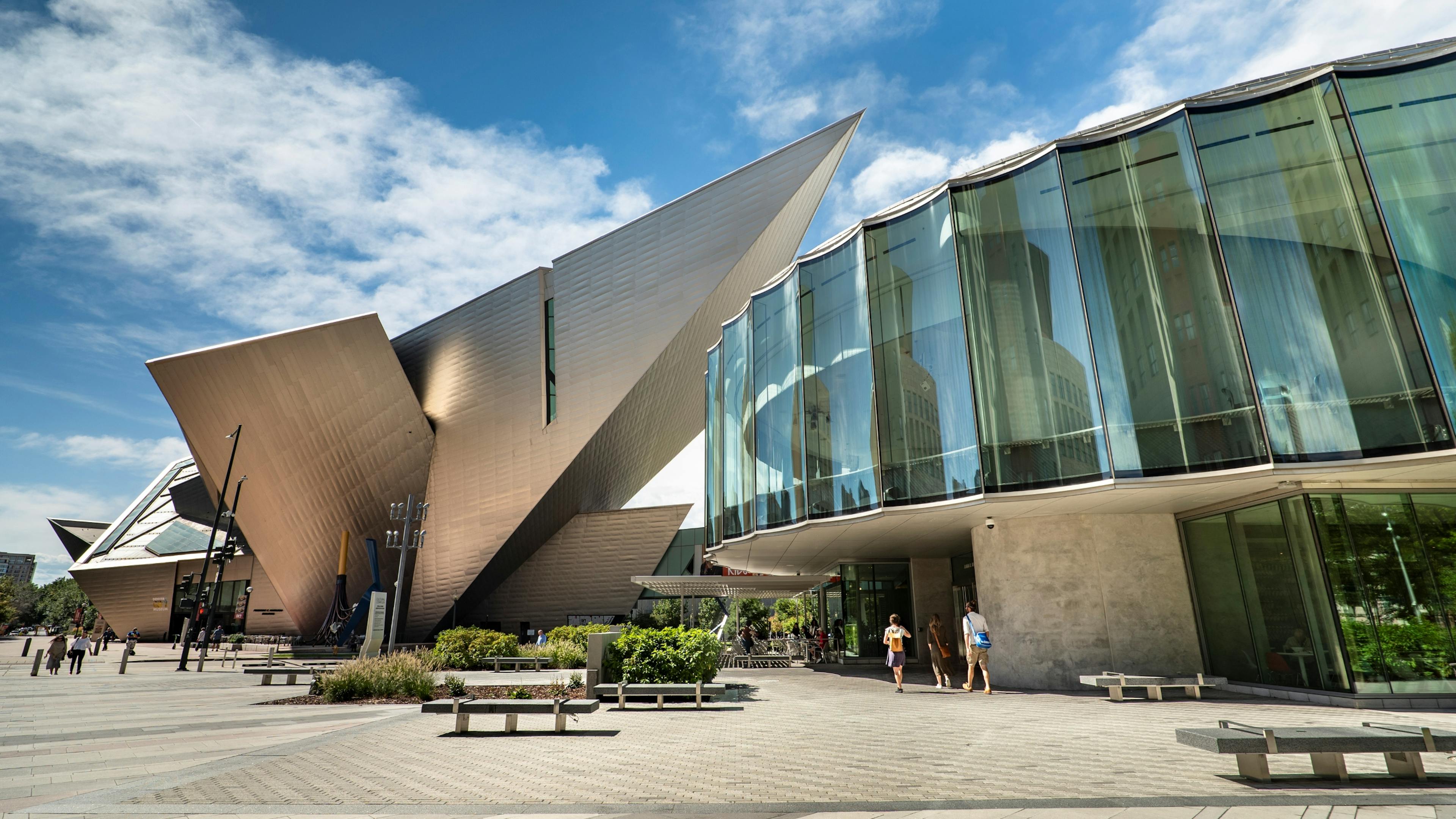 Exterior view of the Denver art museum featuring sharp angles and glass walls under a blue sky.