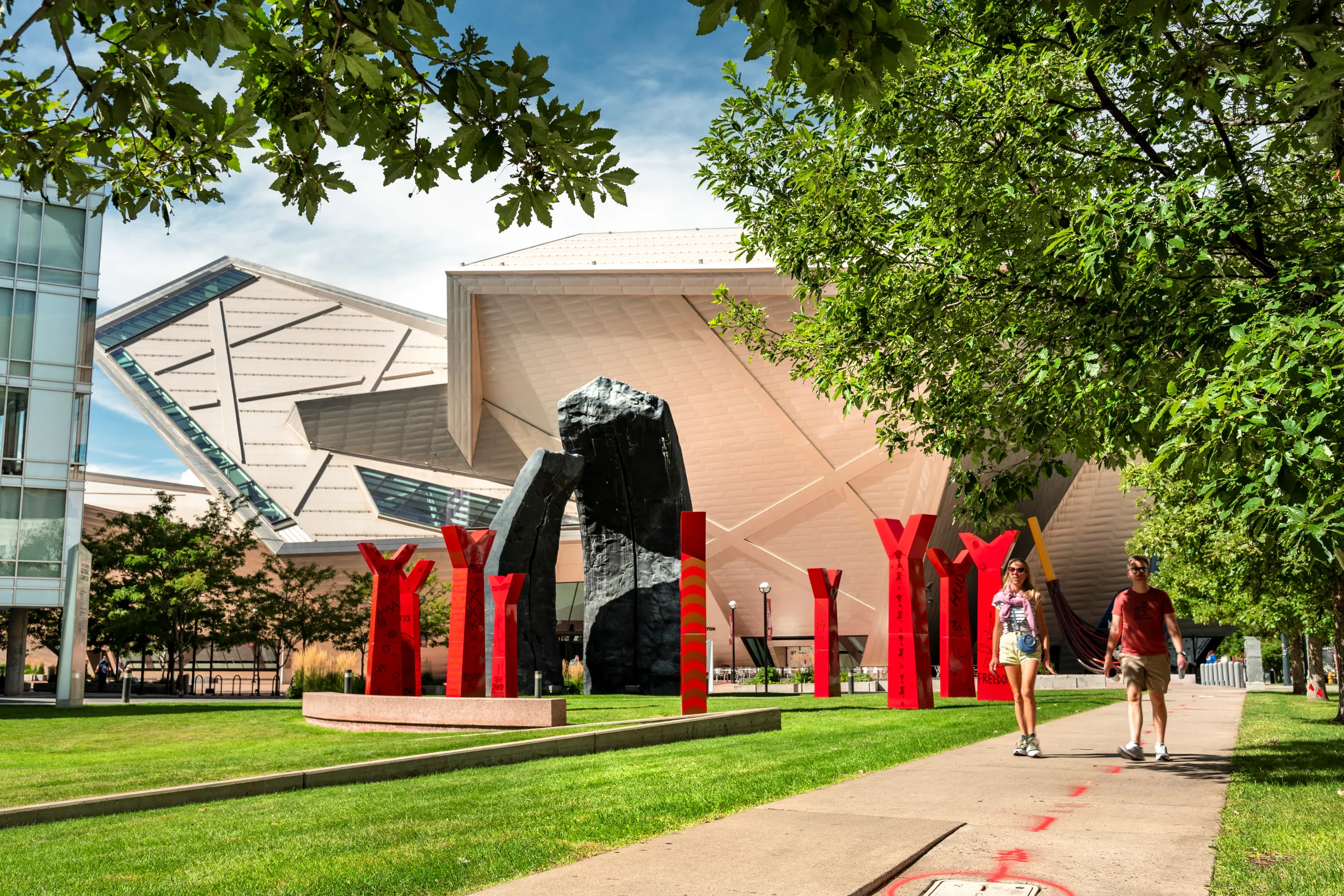 People walking past modern red sculptures and unique architectural buildings in a sunny plaza in the Golden Triangle.