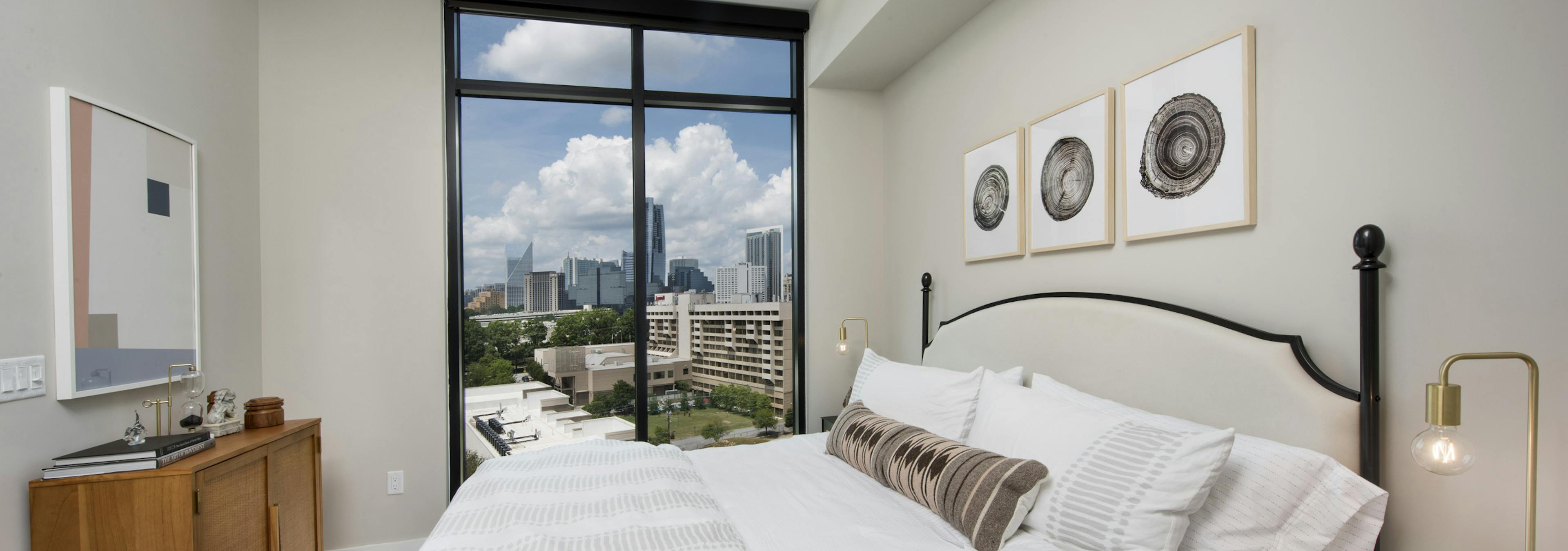 AMLI Lenox bedroom with floor to ceiling windows and a bed with a white comforter and bedside nightstands with lamps