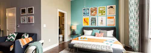 AMLI at Mueller bedroom with a teal accent wall and colorful wall art hanging above bed with peek into connecting bathroom