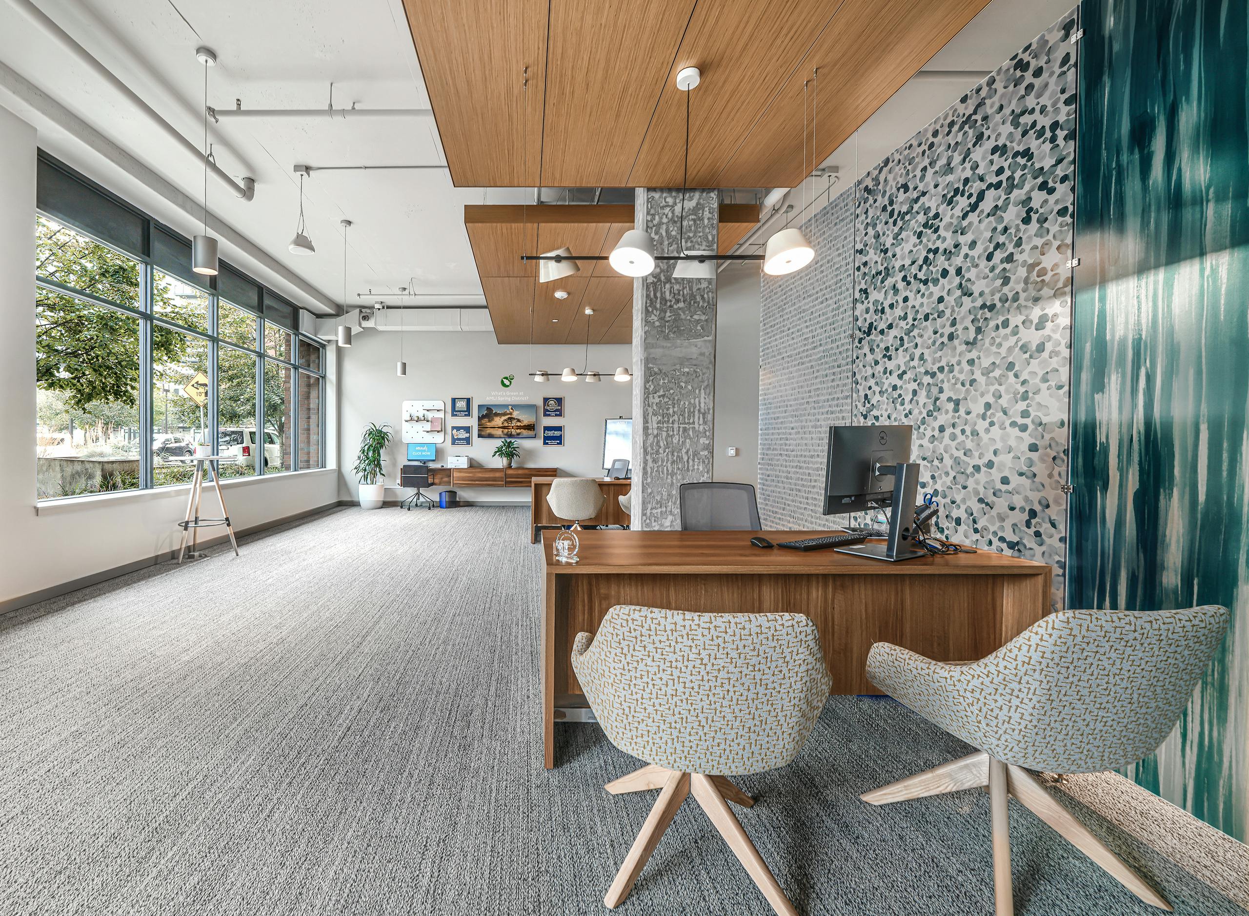 Leasing office at AMLI Spring District with patterned wallpaper and gray pillar and wood desks with chairs and picture window