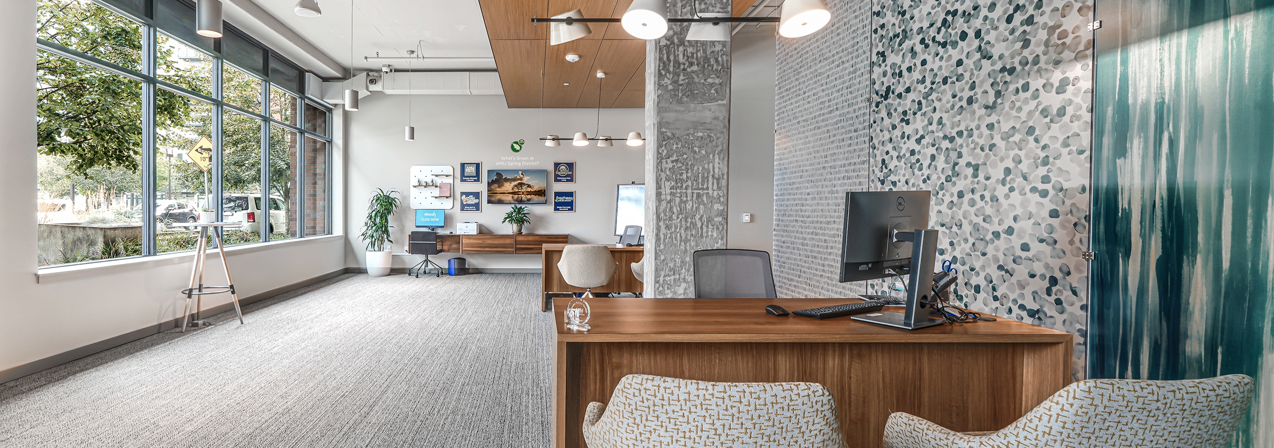 Leasing office at AMLI Spring District with patterned wallpaper and gray pillar and wood desks with chairs and picture window