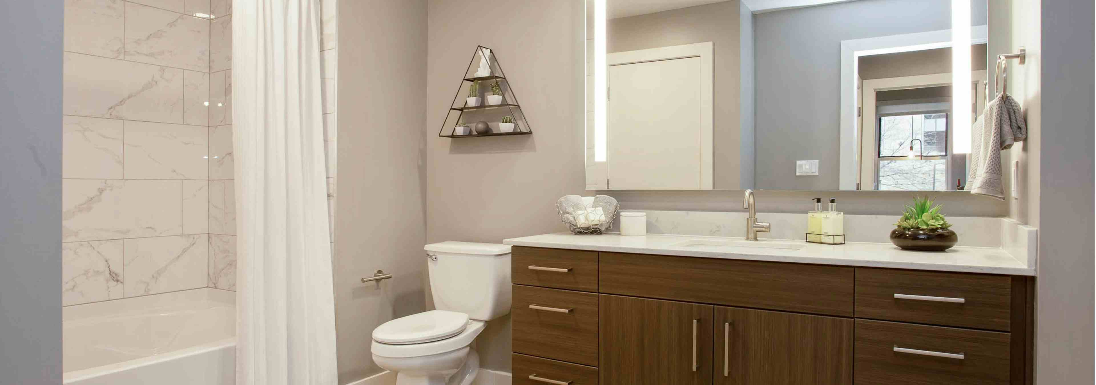 Interior of AMLI Downtown bathroom with shower tub with marble wall tile and a toilet next to a long dark wood vanity sink