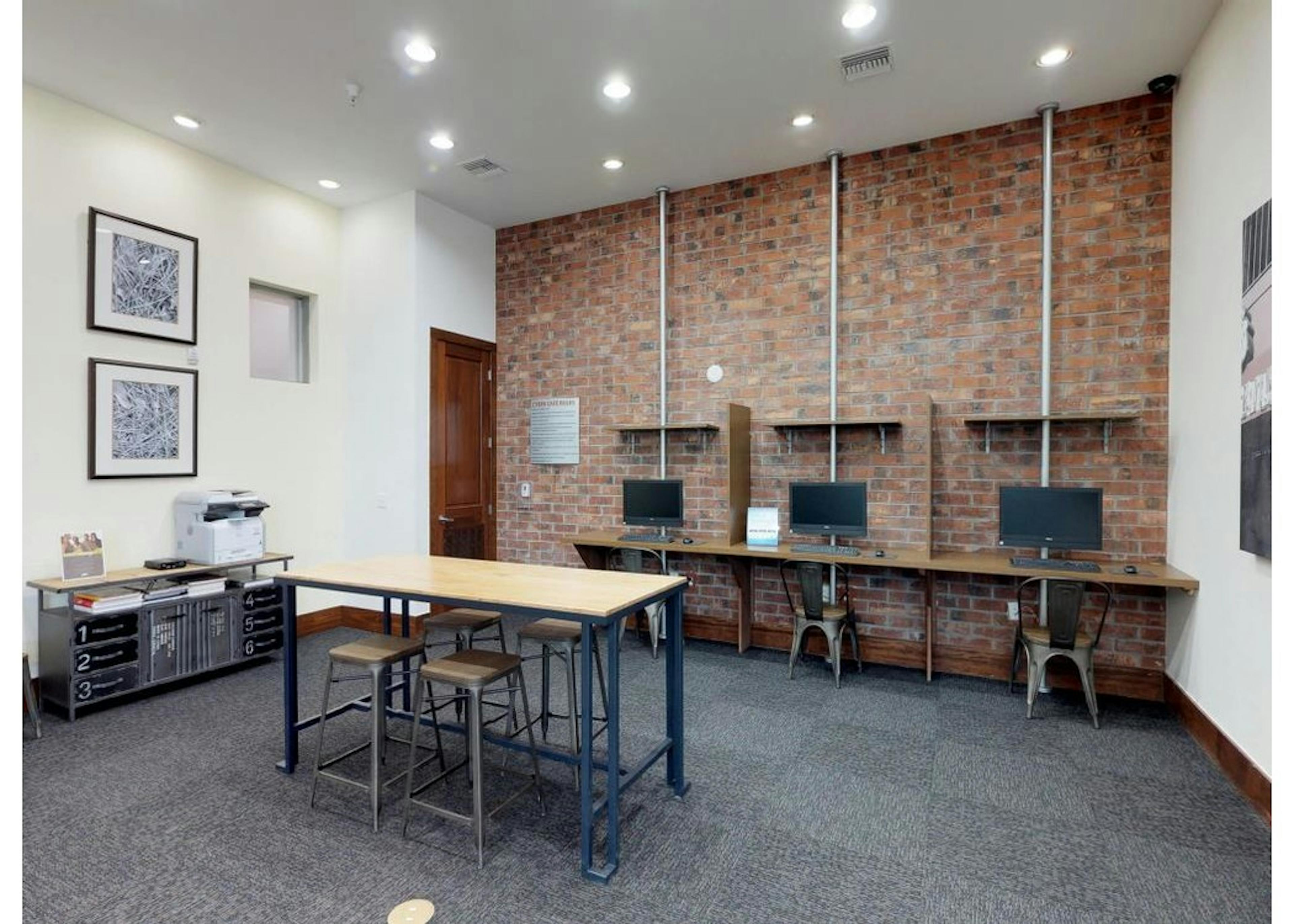 A business center at AMLI Park Avenue apartments with computers and chairs up against a brick wall with a printer and table