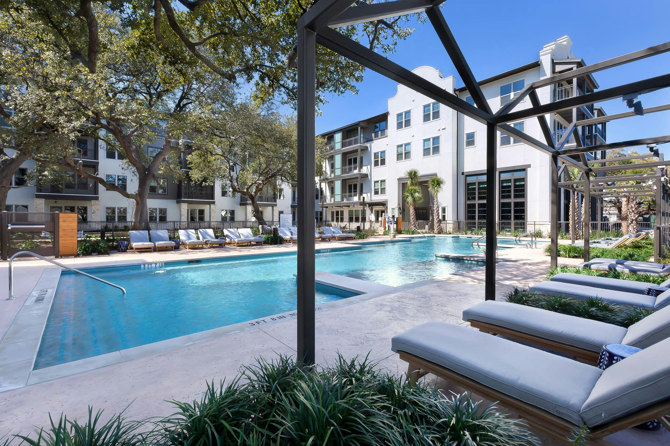 Resort style pool at AMLI Lakeline apartment building with metal cabanas and lounge seating surrounded by lush landscape