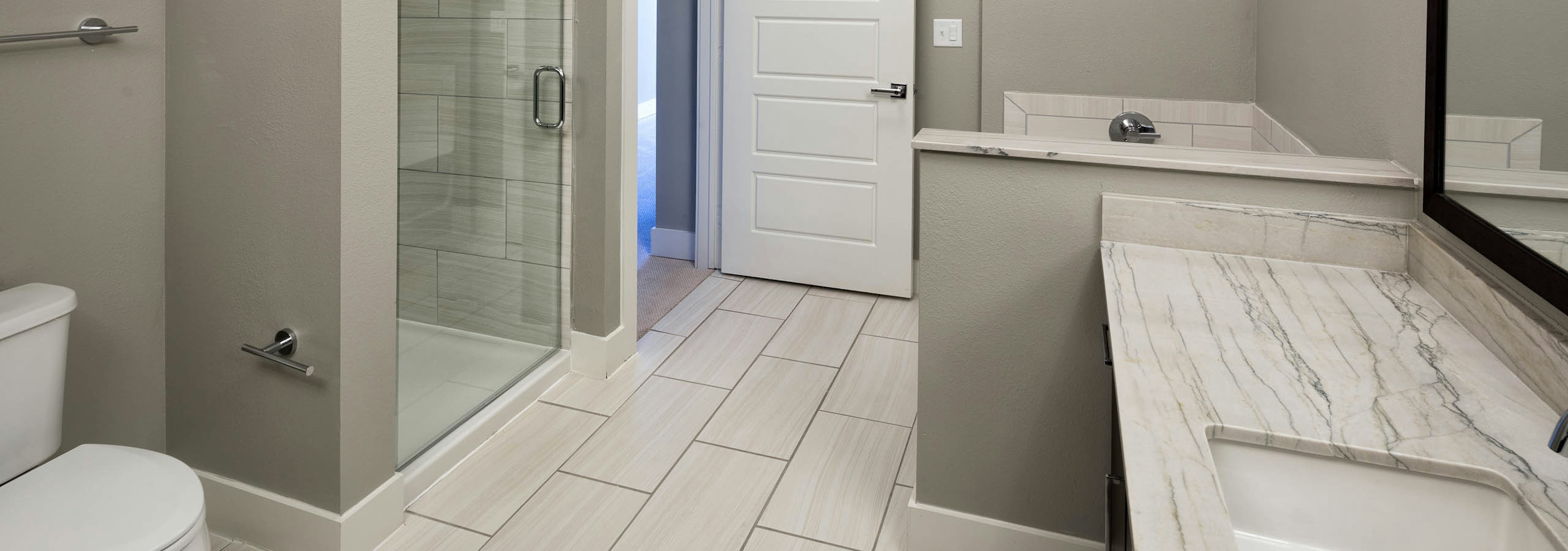 AMLI on Aldrich bathroom featuring glass door shower with white tile floor and short wall separating vanity sink from bathtub