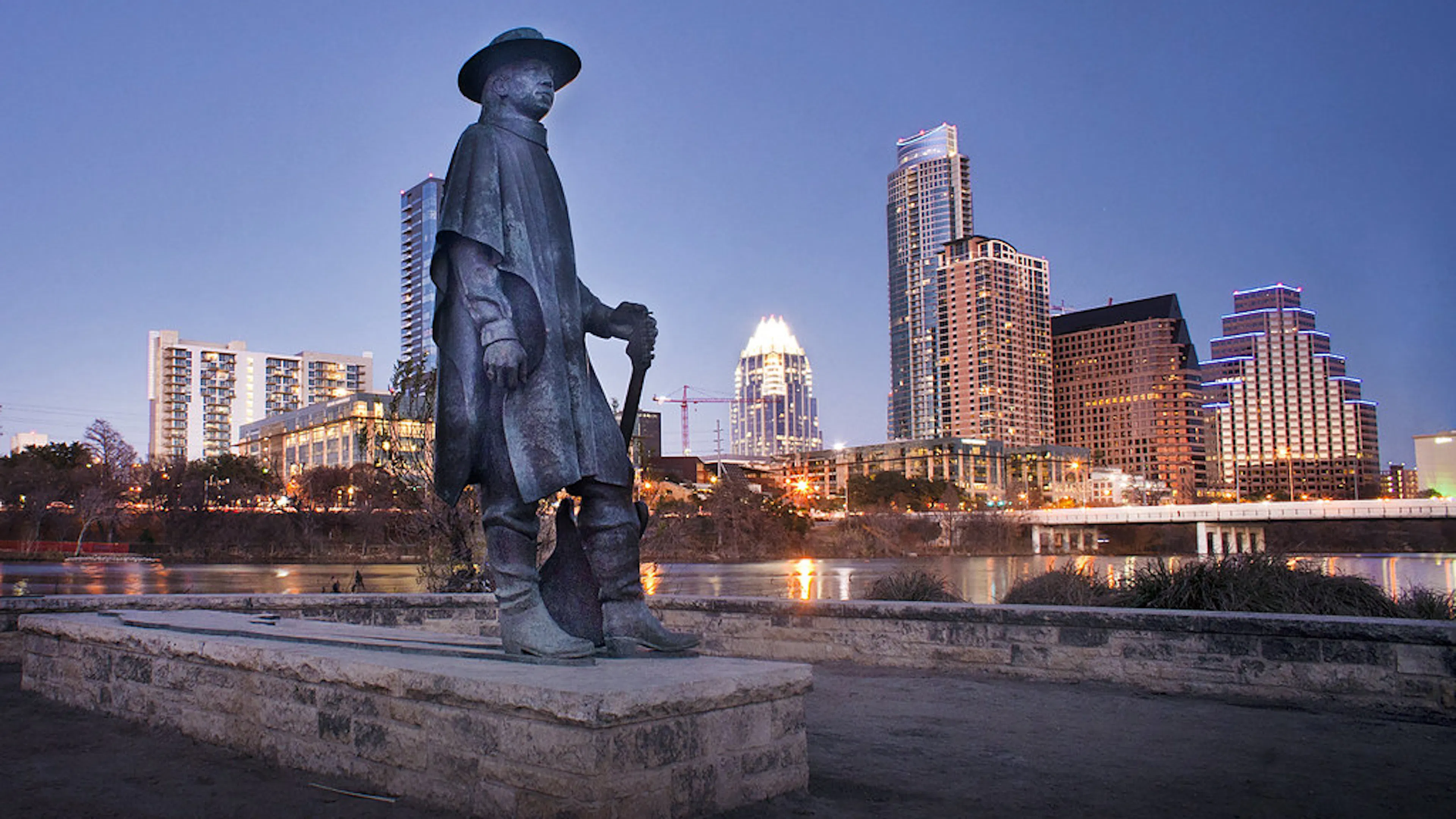 Metal statue of Stevie Ray Vaughan with the Downtown Austin skyline lit up in the background