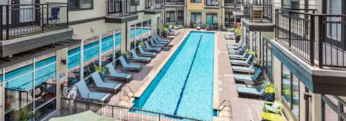 Exterior view of AMLI 5350 pool area with two long thin swimming pools separated by blue lounge chairs on cement