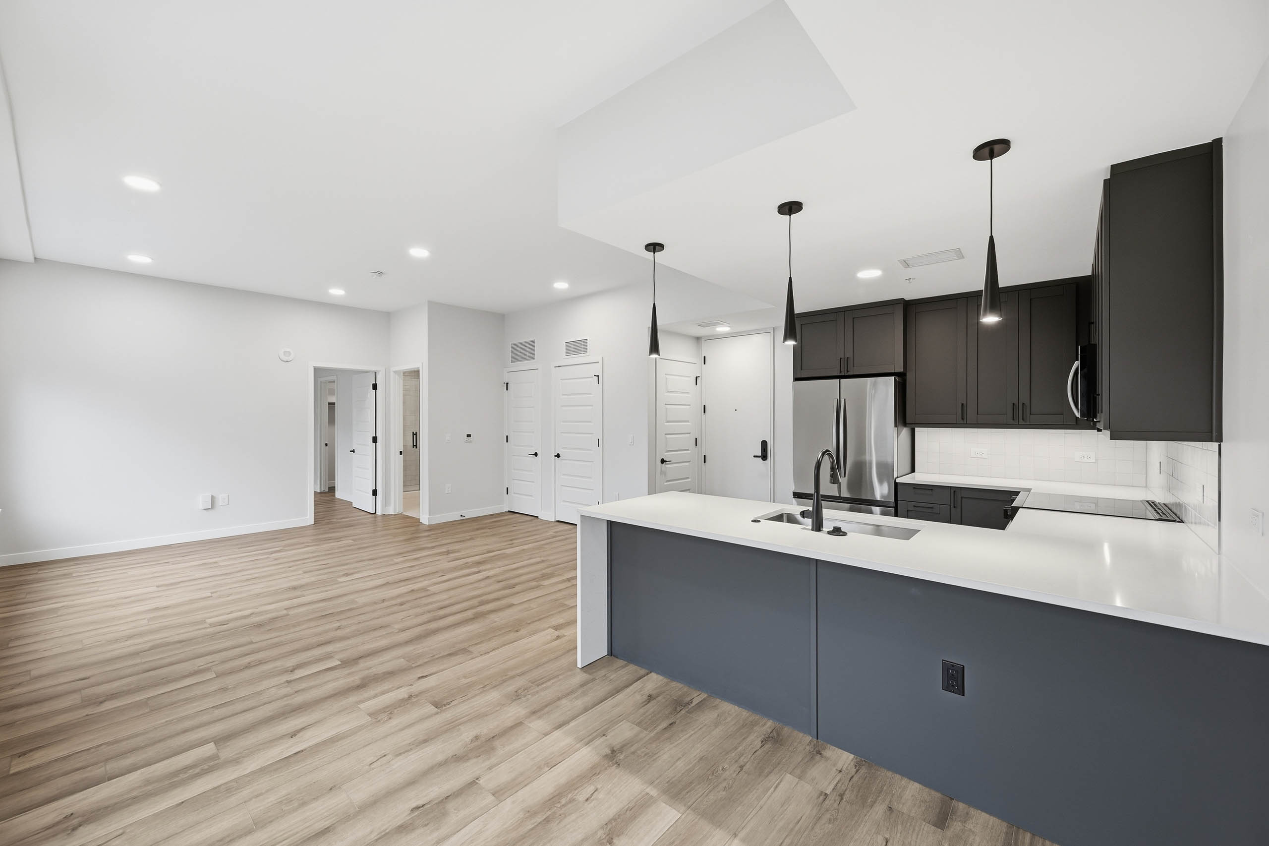 Open kitchen and living area at AMLI Golden Triangle with wood floors and dark cabinets with stainless steel appliances and pendant lights.