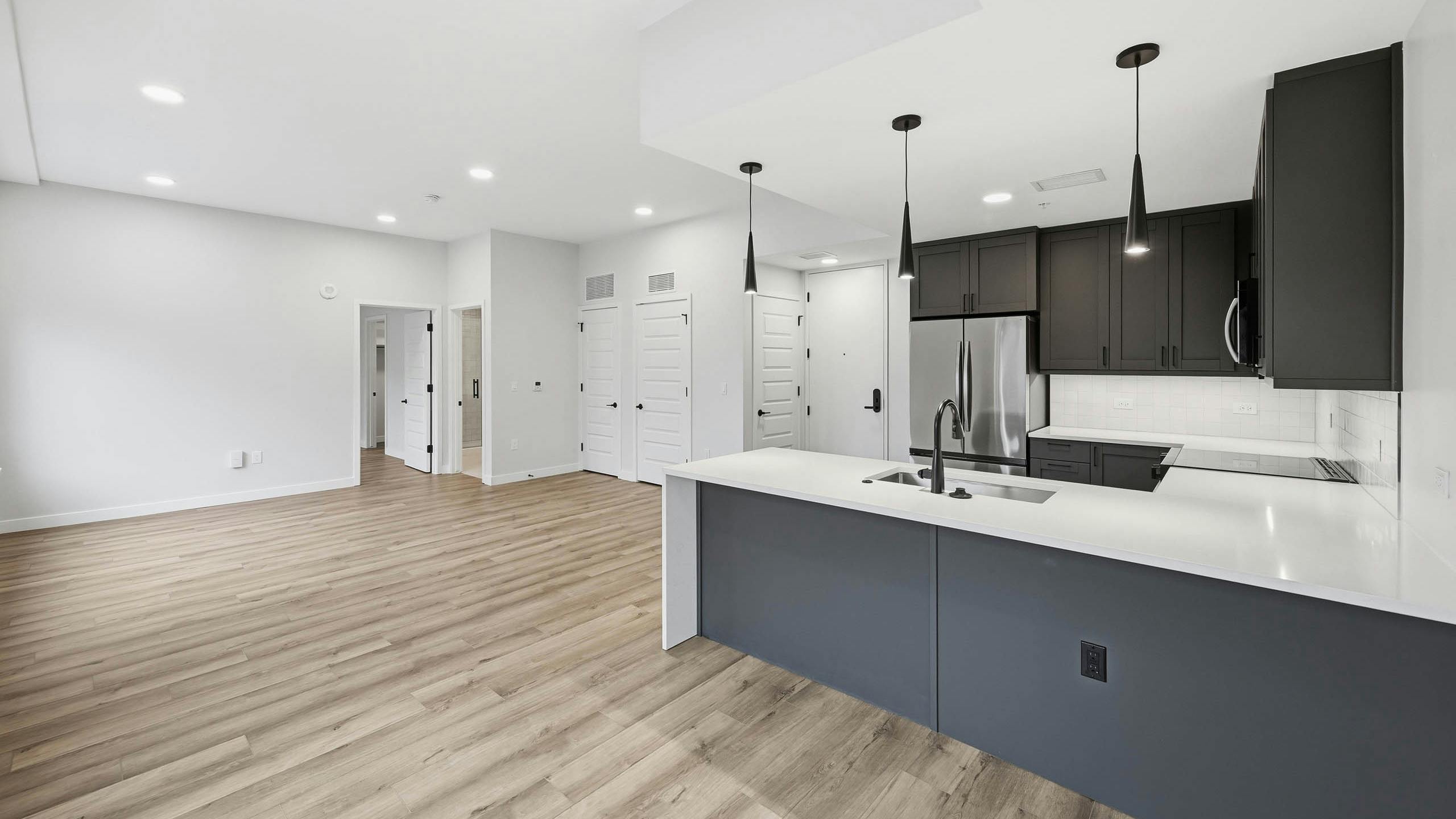 Open kitchen and living area at AMLI Golden Triangle with wood floors and dark cabinets with stainless steel appliances and pendant lights.