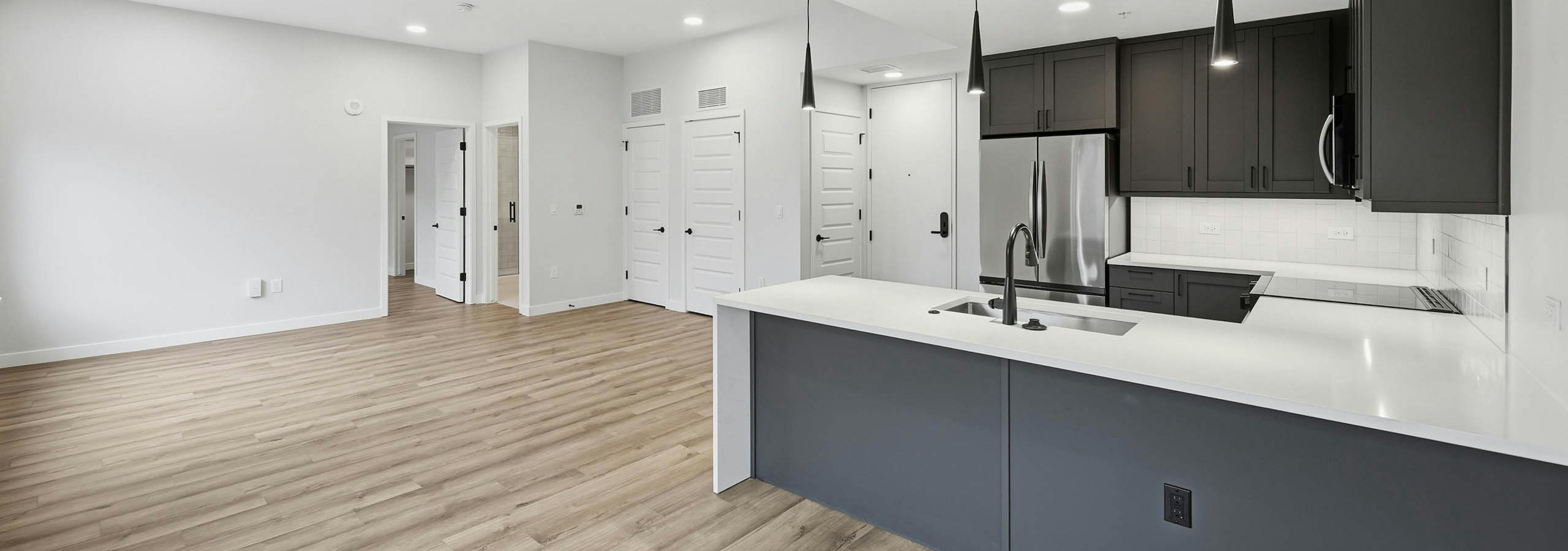 Open kitchen and living area at AMLI Golden Triangle with wood floors and dark cabinets with stainless steel appliances and pendant lights.