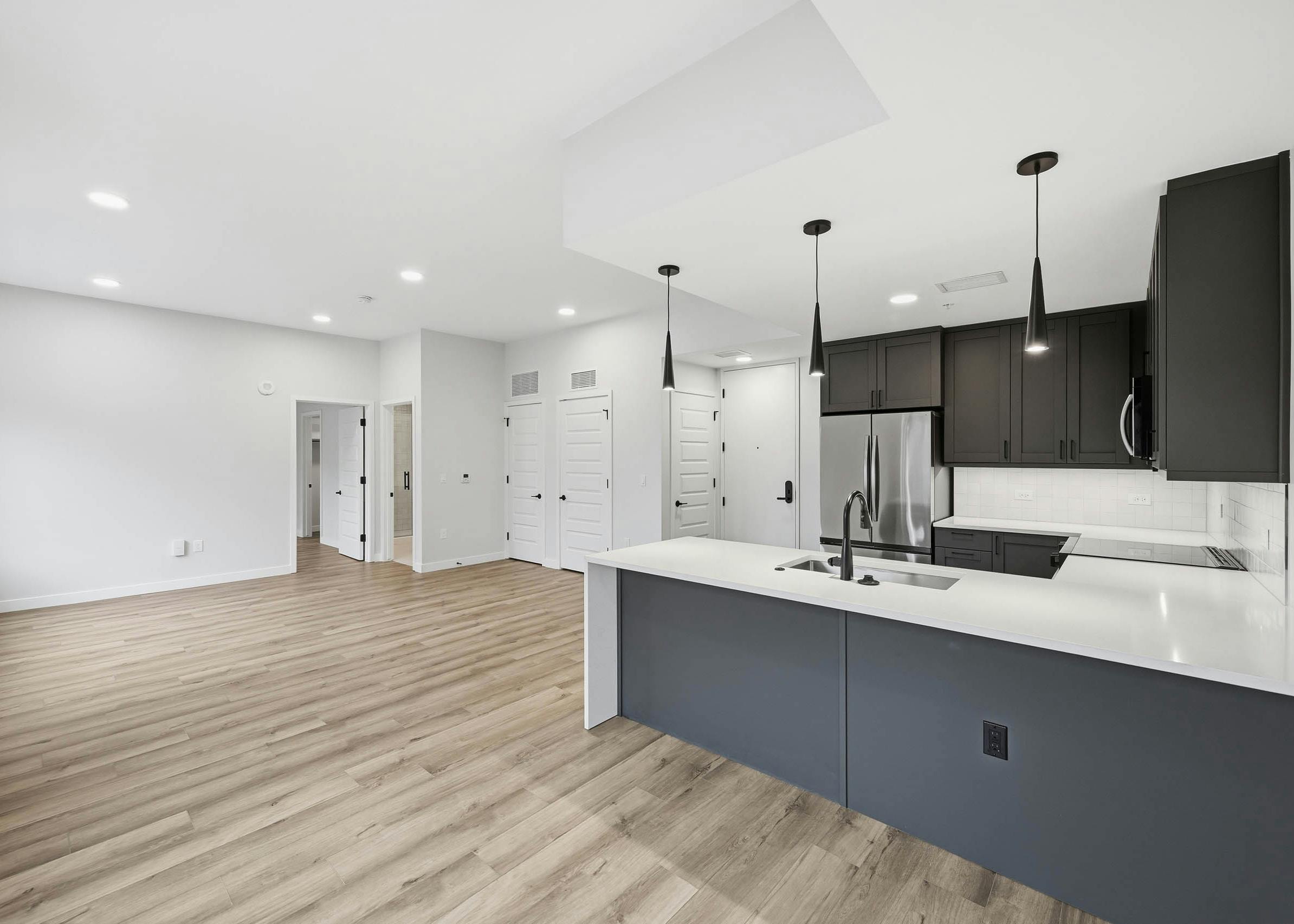 Open kitchen and living area at AMLI Golden Triangle with wood floors and dark cabinets with stainless steel appliances and pendant lights.