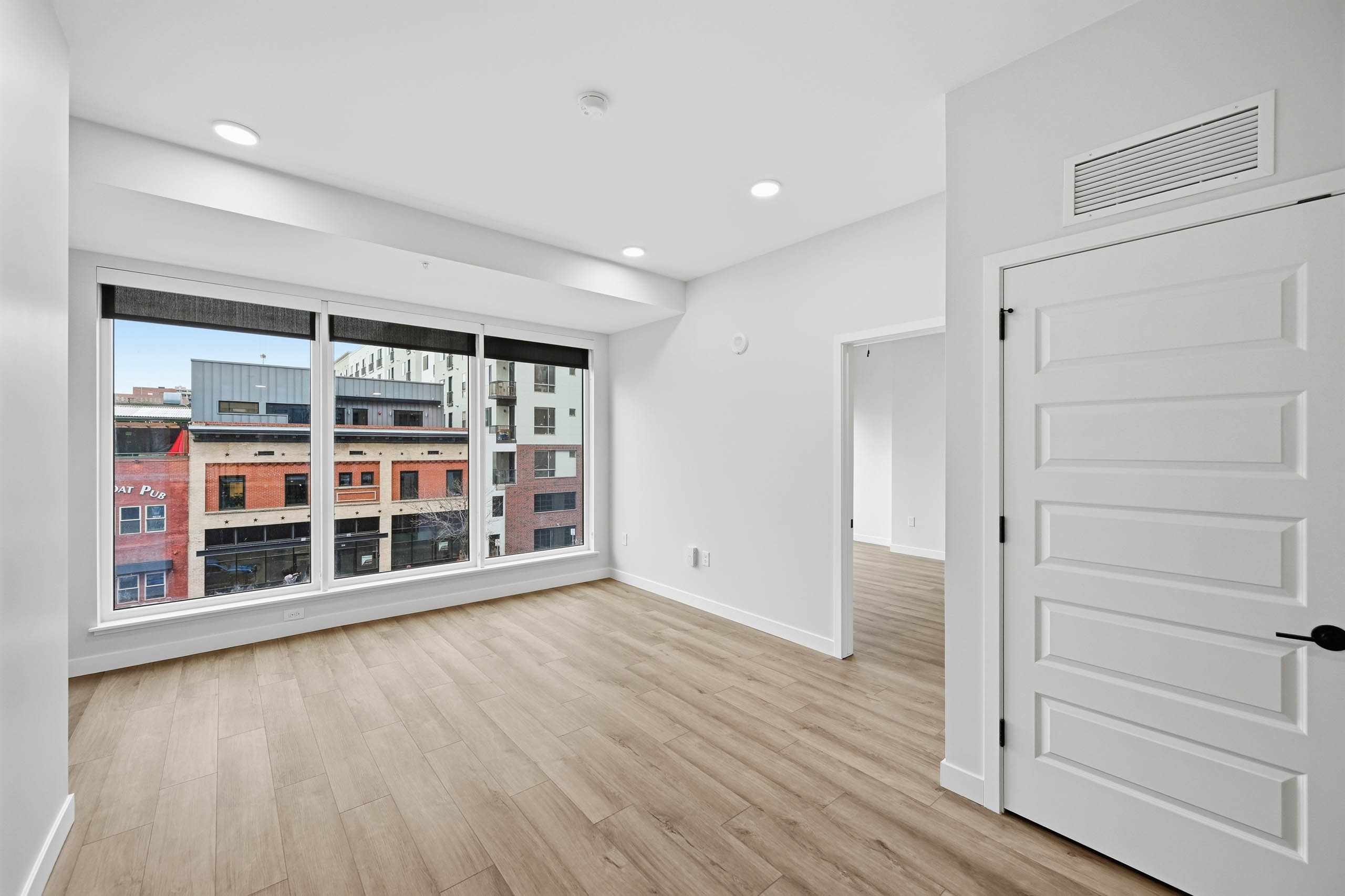 AMLI Golden Triangle interior living area with wood flooring and recessed lighting and large windows showing city views.