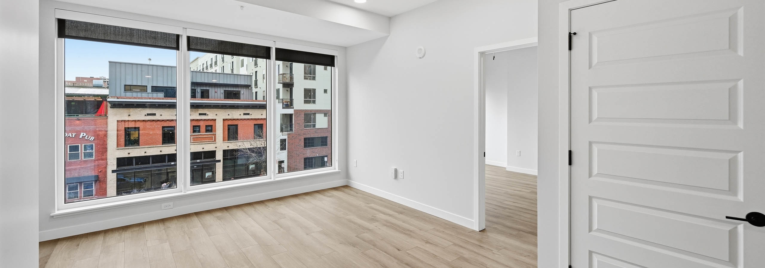AMLI Golden Triangle interior living area with wood flooring and recessed lighting and large windows showing city views.