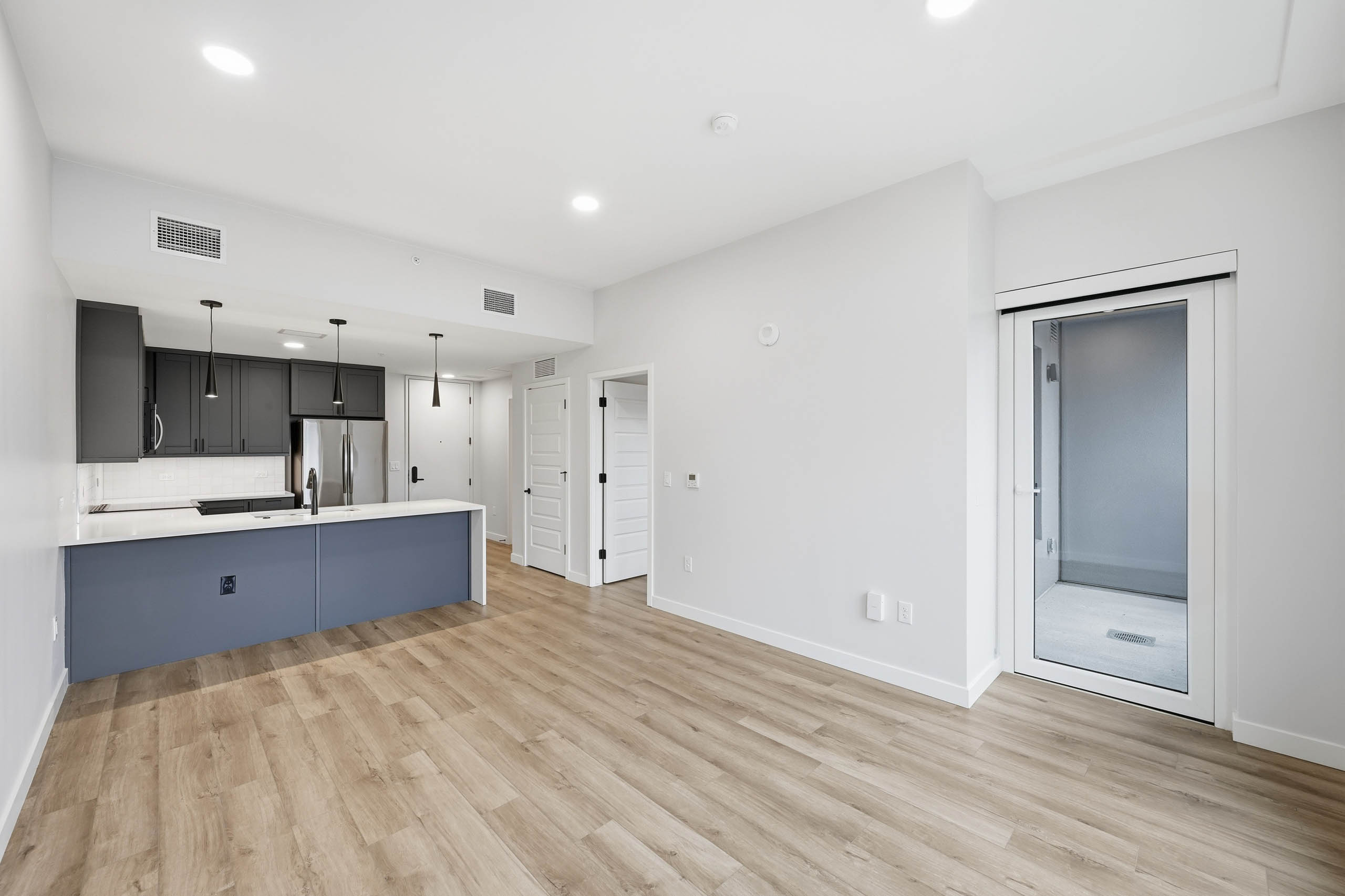 Interior view of living room at AMLI Golden Triangle with light wood floors, an open kitchen with dark cabinets and white countertop.