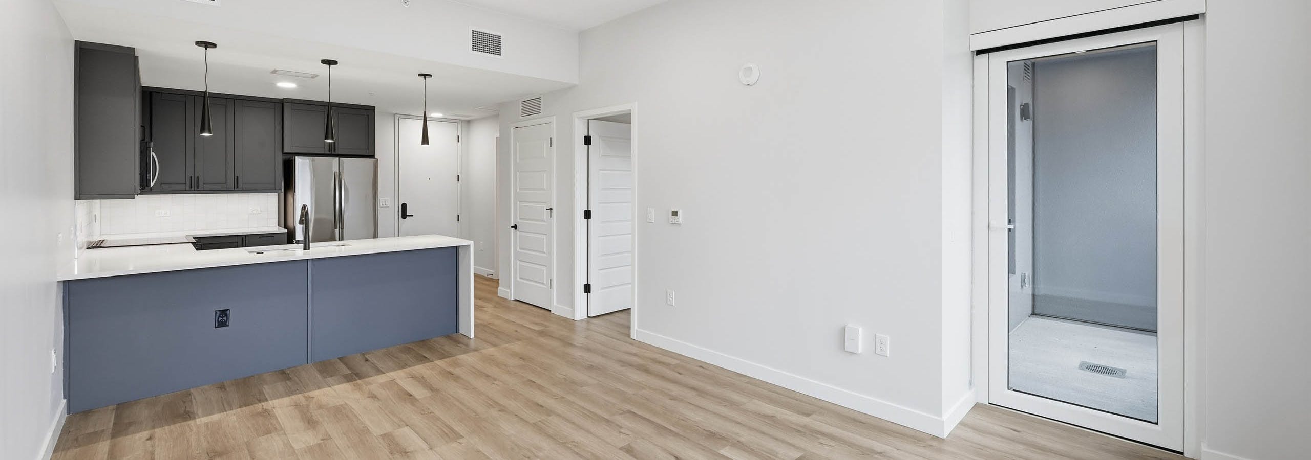 Interior view of living room at AMLI Golden Triangle with light wood floors, an open kitchen with dark cabinets and white countertop.