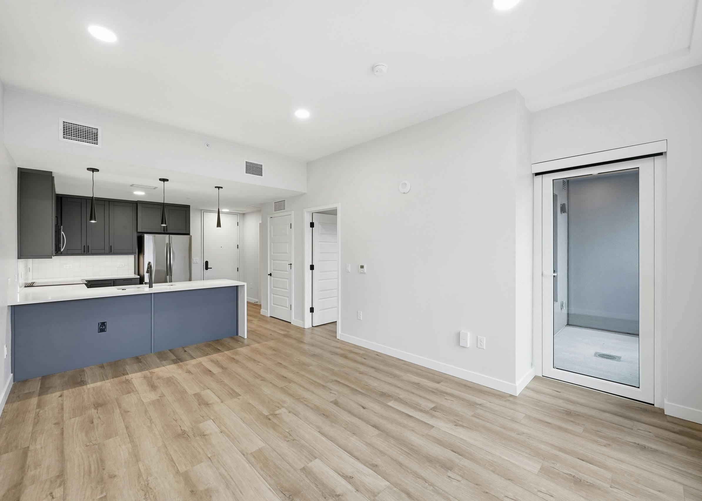 Interior view of living room at AMLI Golden Triangle with light wood floors, an open kitchen with dark cabinets and white countertop.