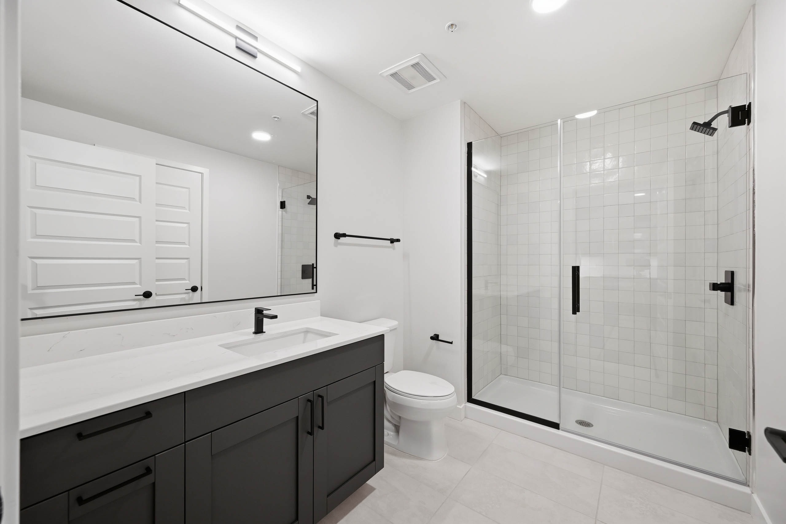 Modern bathroom with dark vanity, white countertop and a glass-enclosed shower with black fixtures at AMLI Golden Triangle.
