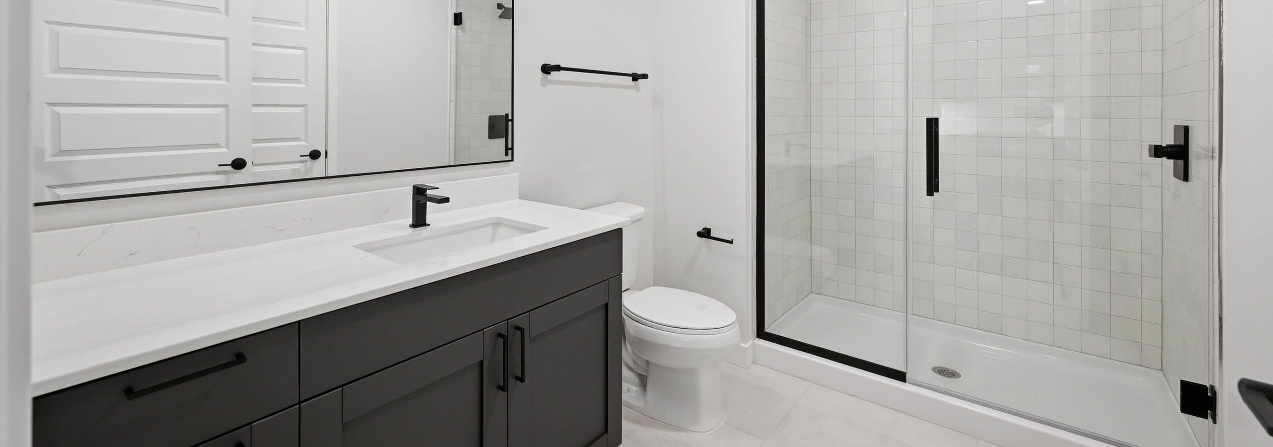 Modern bathroom with dark vanity, white countertop and a glass-enclosed shower with black fixtures at AMLI Golden Triangle.