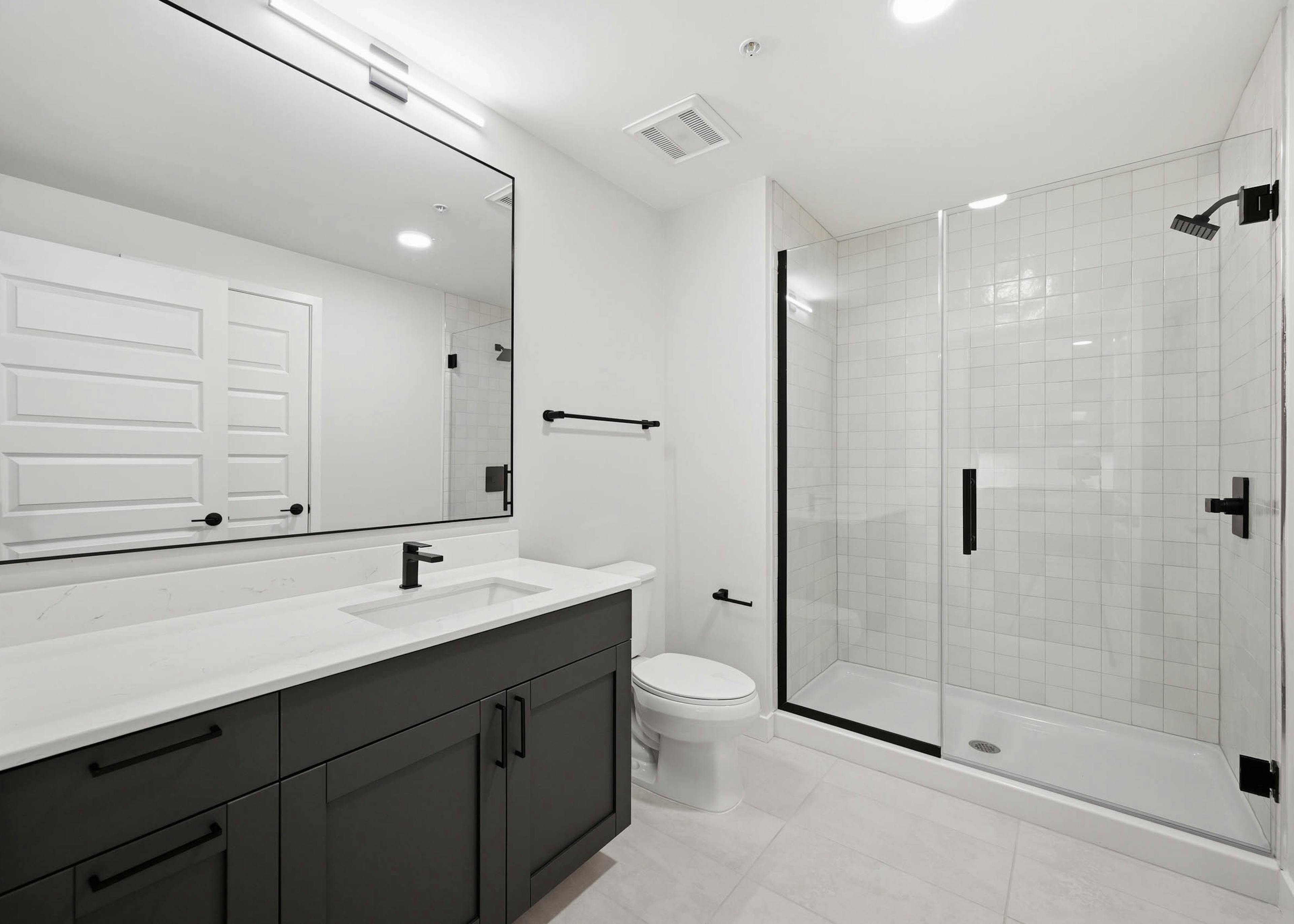 Modern bathroom with dark vanity, white countertop and a glass-enclosed shower with black fixtures at AMLI Golden Triangle.