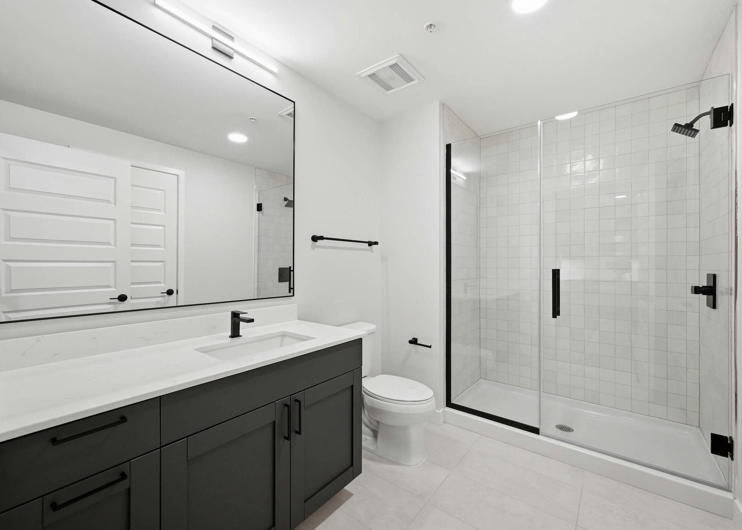 Modern bathroom with dark vanity, white countertop and a glass-enclosed shower with black fixtures at AMLI Golden Triangle.