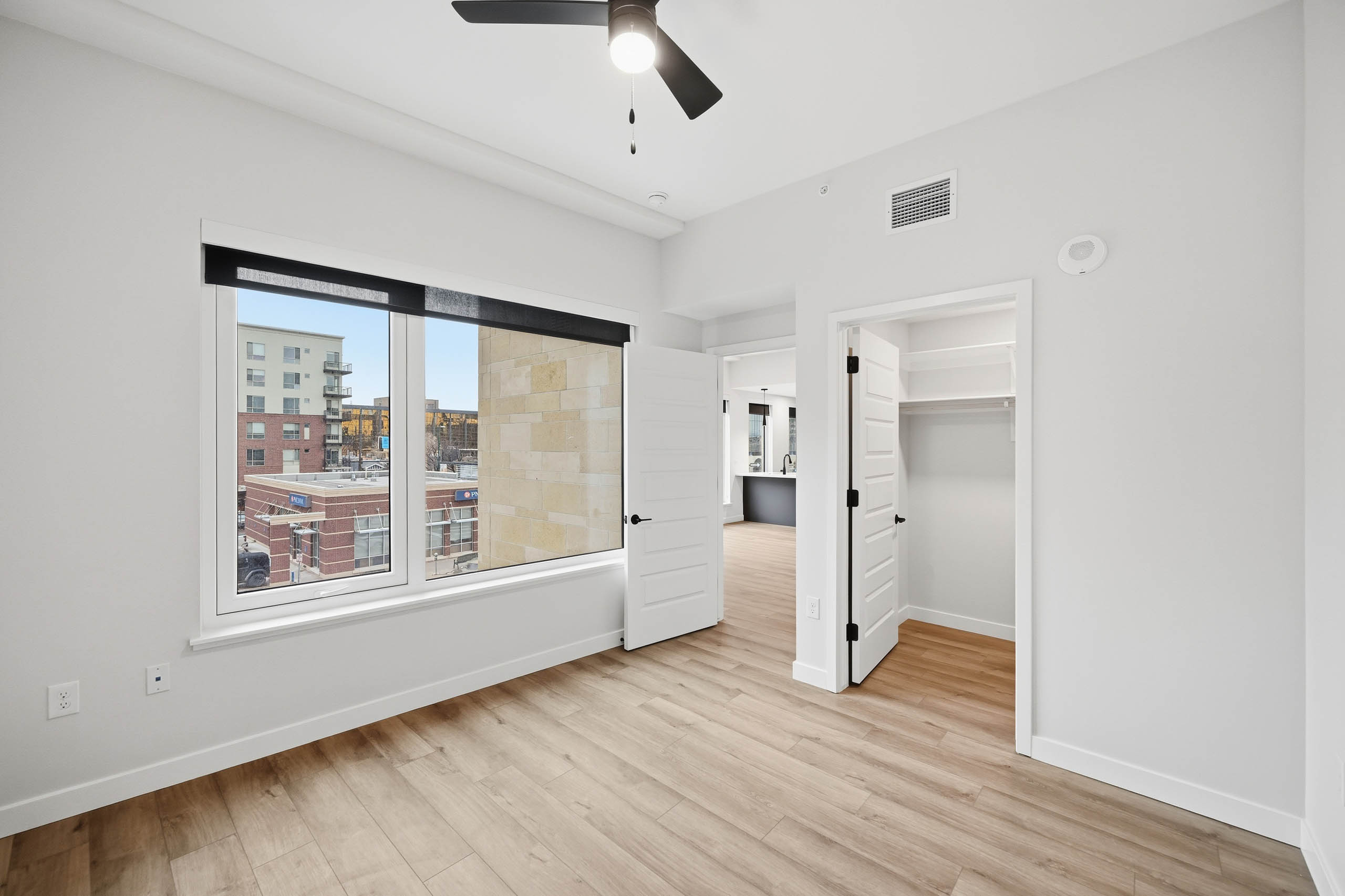 AMLI Golden Triangle apartment bedroom with light wood floors and a ceiling fan and large window with city view.