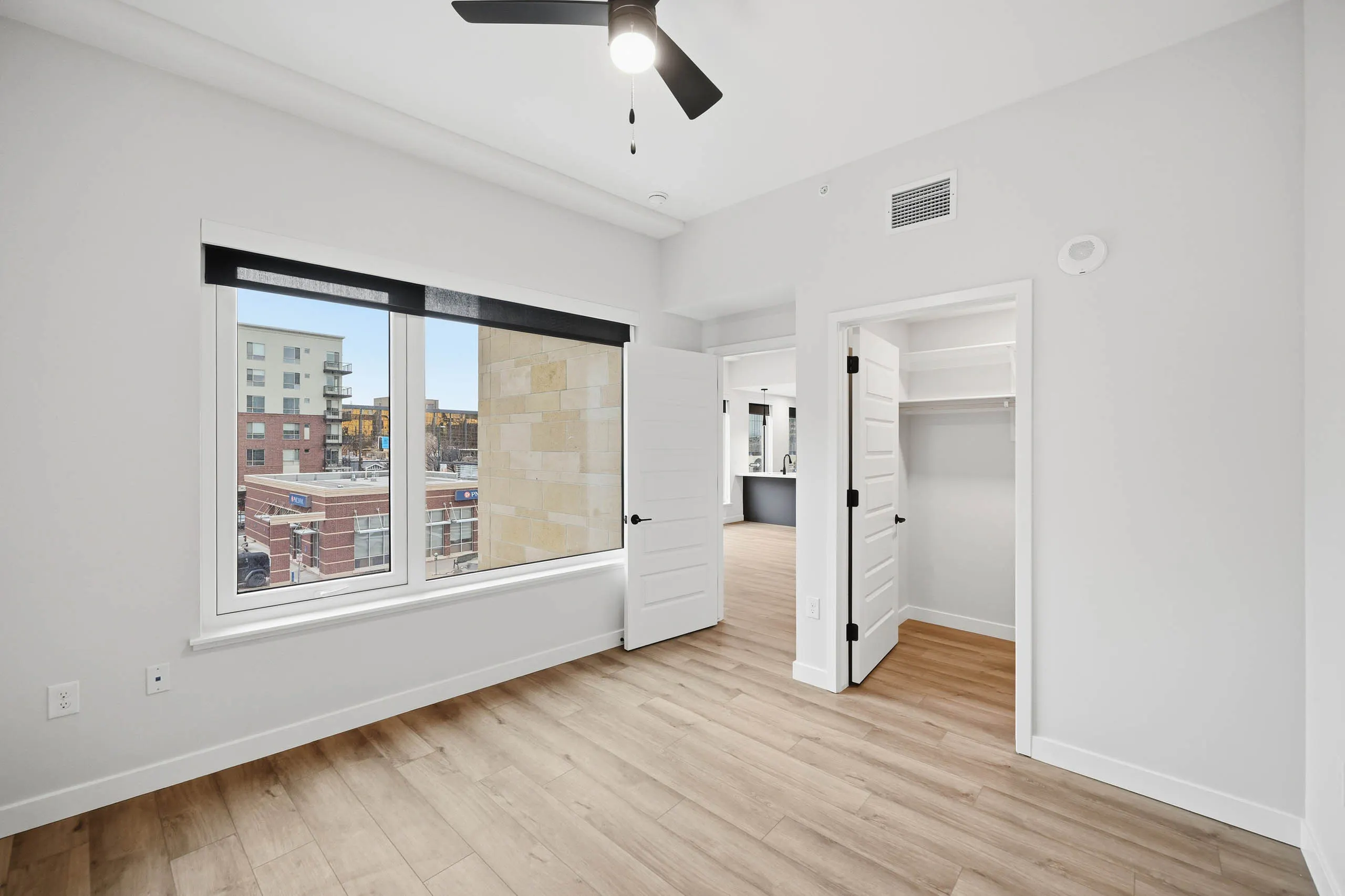 AMLI Golden Triangle apartment bedroom with light wood floors and a ceiling fan and large window with city view.