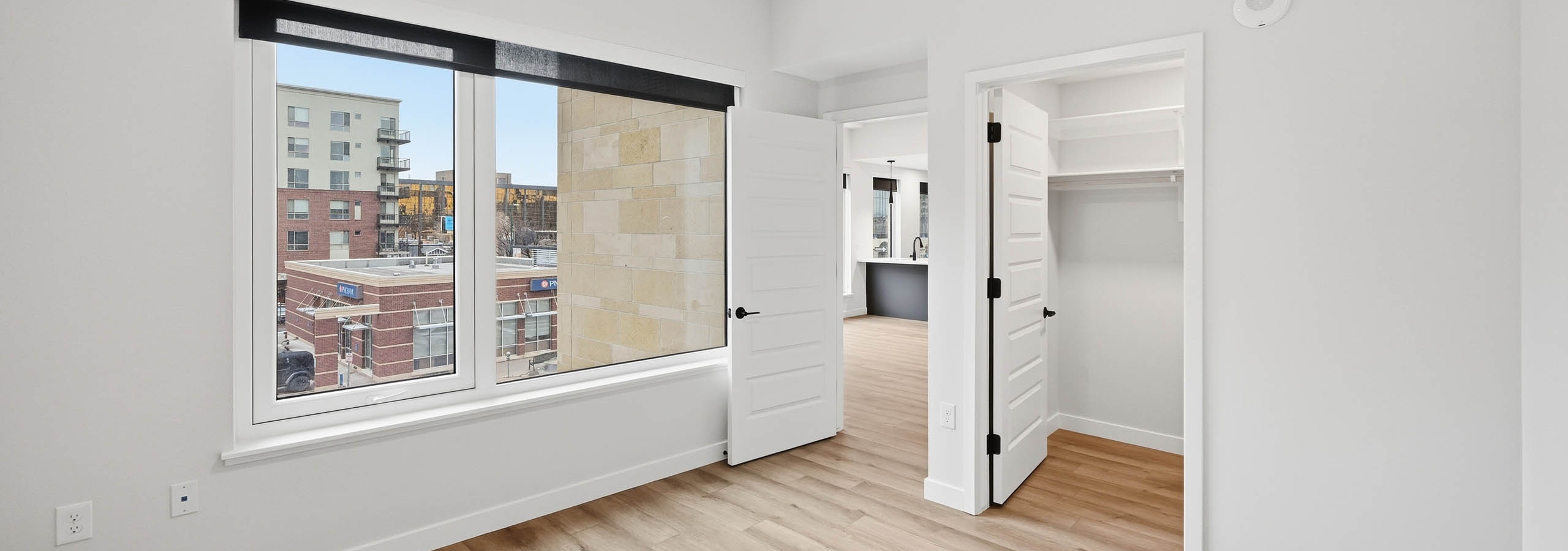 AMLI Golden Triangle apartment bedroom with light wood floors and a ceiling fan and large window with city view.