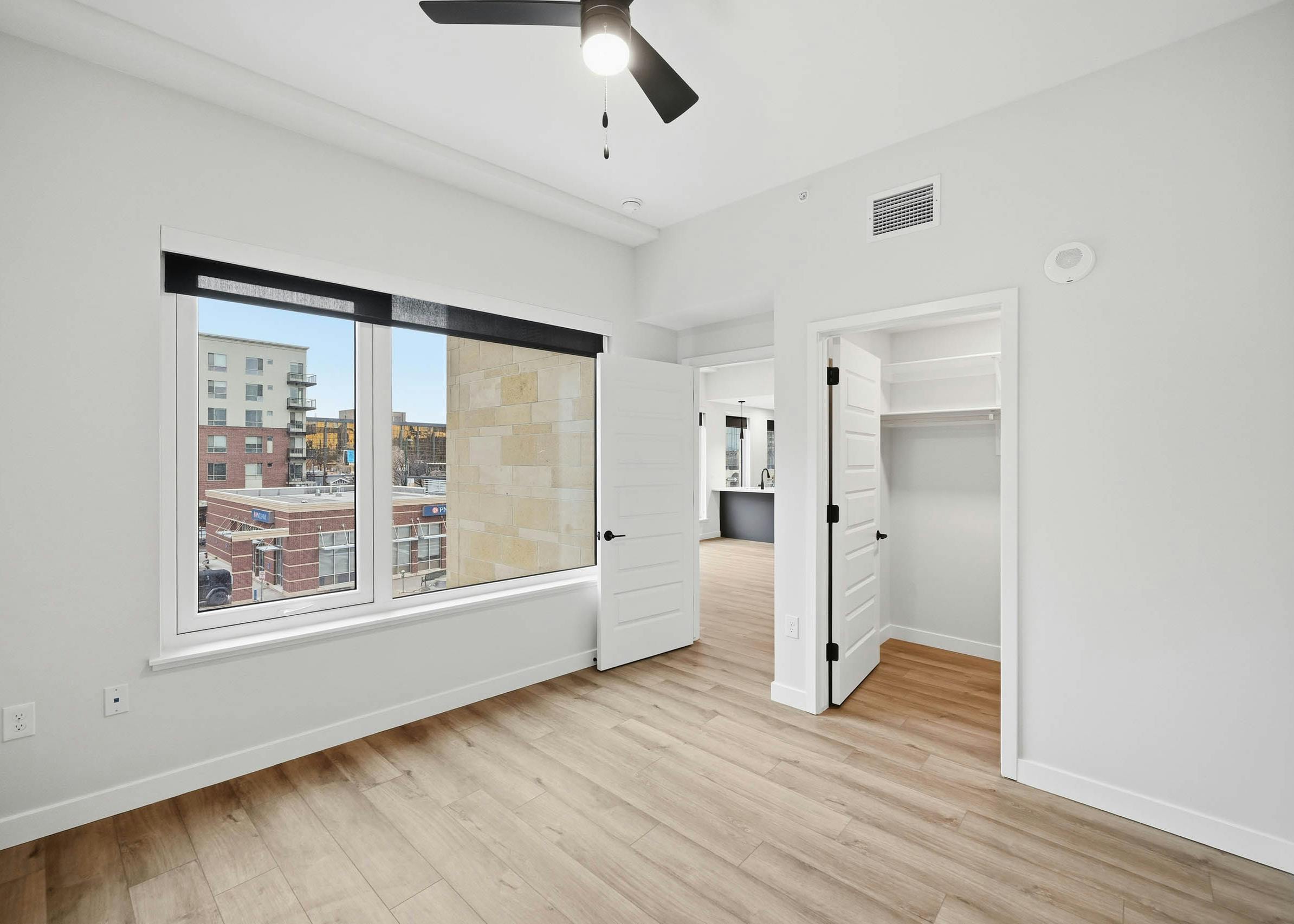 AMLI Golden Triangle apartment bedroom with light wood floors and a ceiling fan and large window with city view.