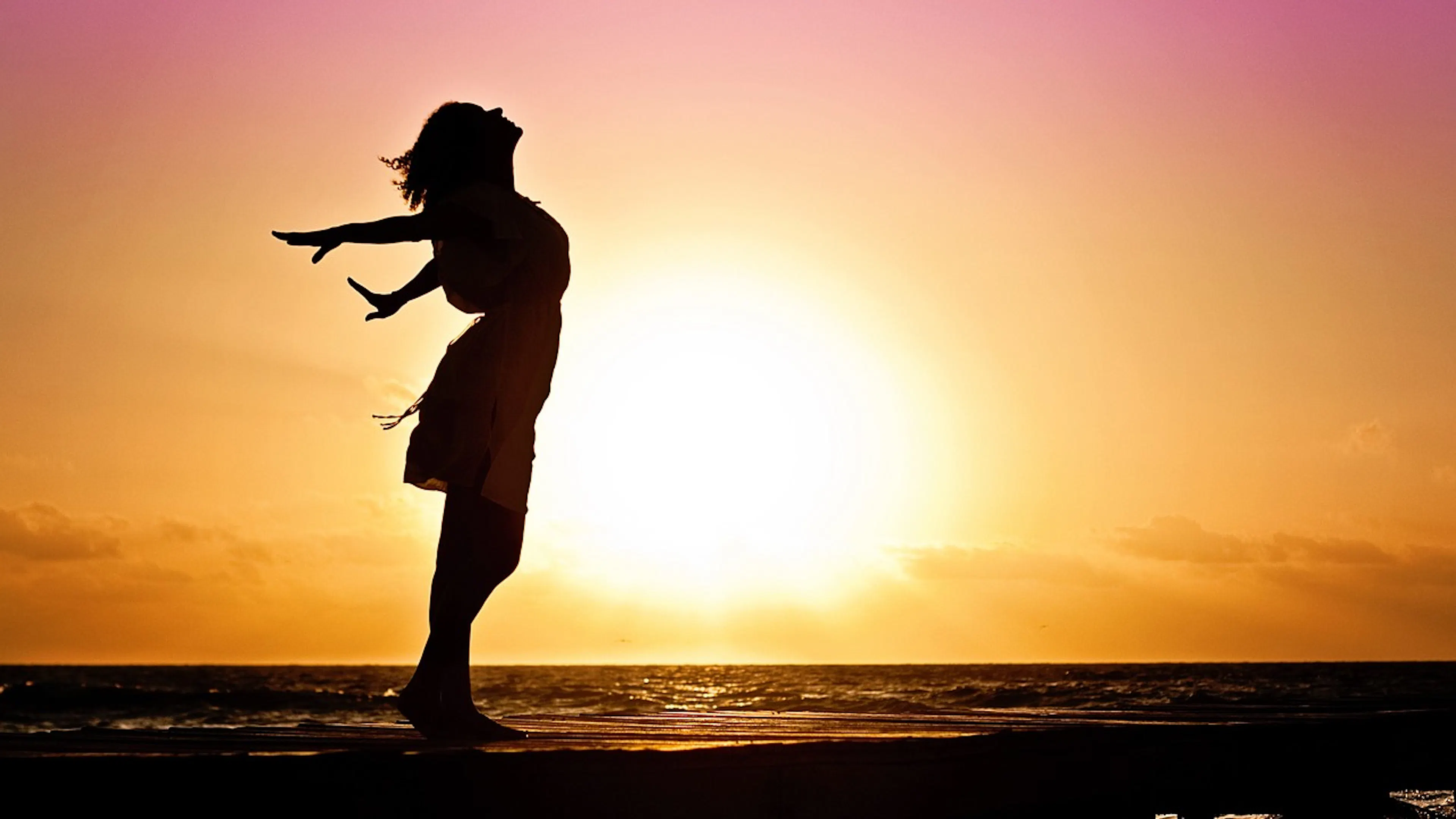 Silhouette of woman standing in front of a sunset and water in background