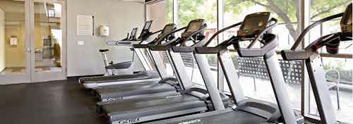 Interior daytime view of AMLI Warner Center apartment building workout facility with cardio equipment facing pool courtyard