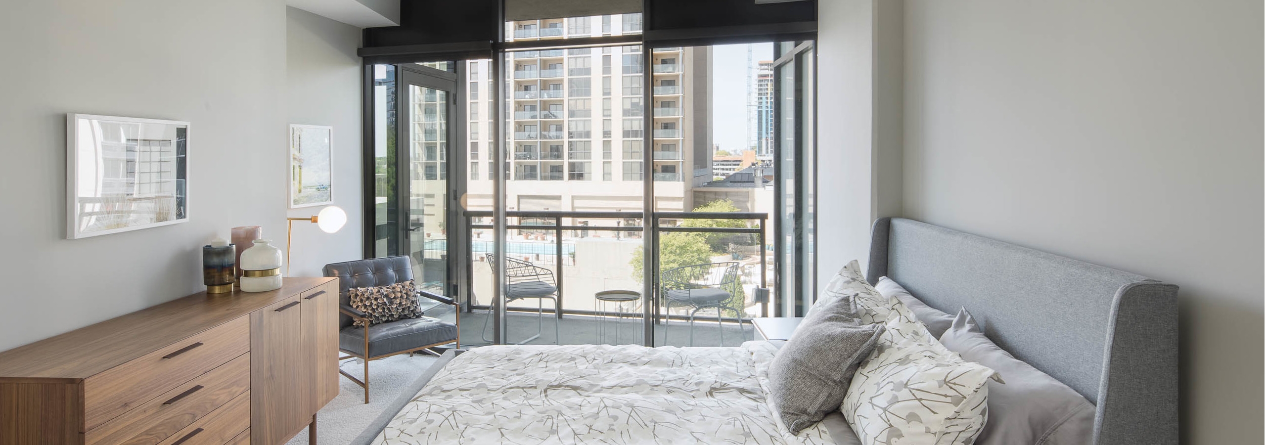 AMLI Arts Center bedroom with neutral walls and white patterned bedding with bright city view out of floor to ceiling windows