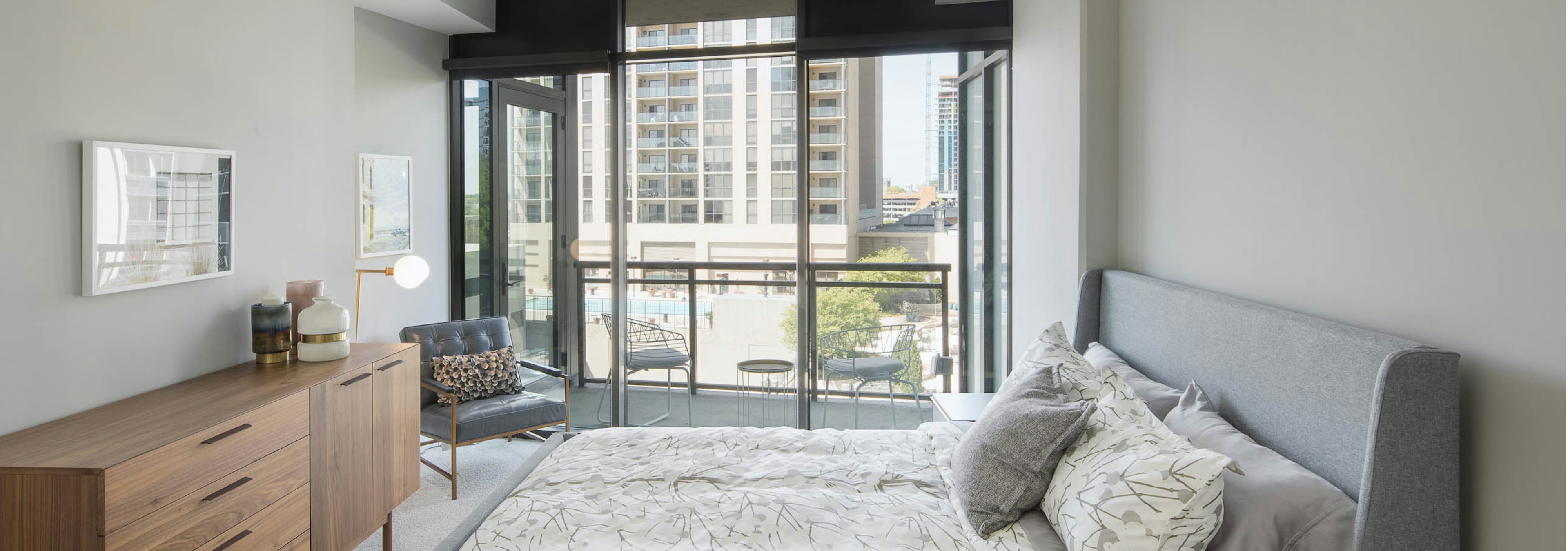 AMLI Arts Center bedroom with neutral walls and white patterned bedding with bright city view out of floor to ceiling windows