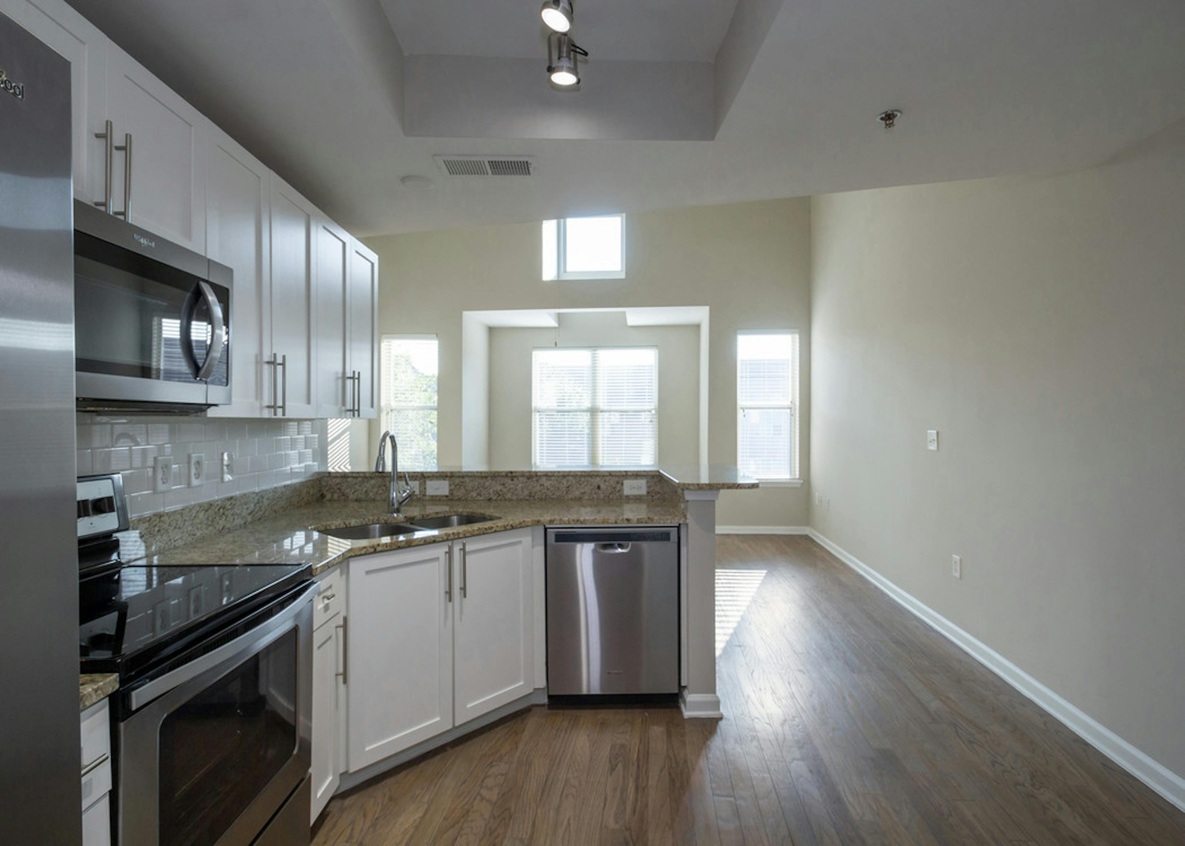 Interior view of AMLI Lindbergh apartment kitchen with white cabinets, granite countertops, and stainless steel appliances