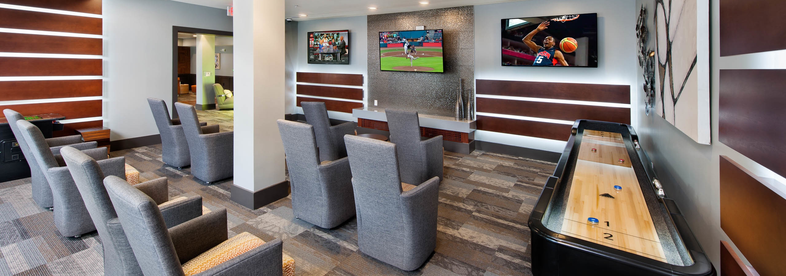 Interior view of the media room at AMLI Piedmont Heights with grey seating facing multiple large TVs on the wall