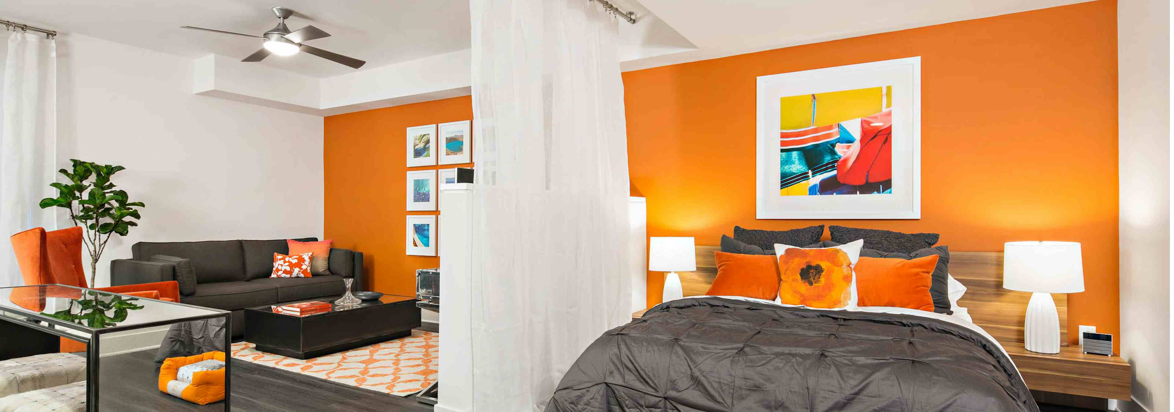 Interior of AMLI Lex on Orange furnished studio apartment with orange wall, queen bed, gray couch and coffee and dining table