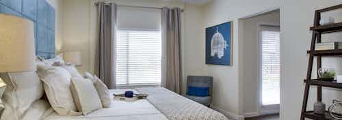 AMLI Ponce Park apartment bedroom with cream walls and dark hardwood flooring with large windows for natural sunlight