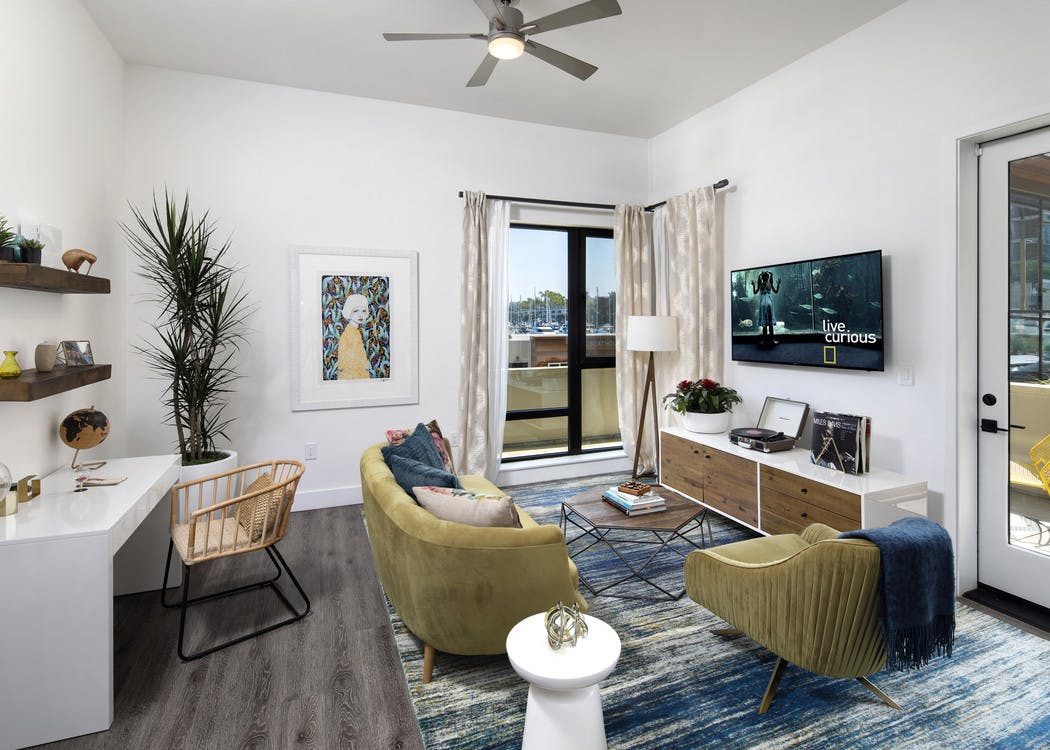 Interior of AMLI Marina Del Rey model living room with couch, coffee table and desk in front of large window facing marina