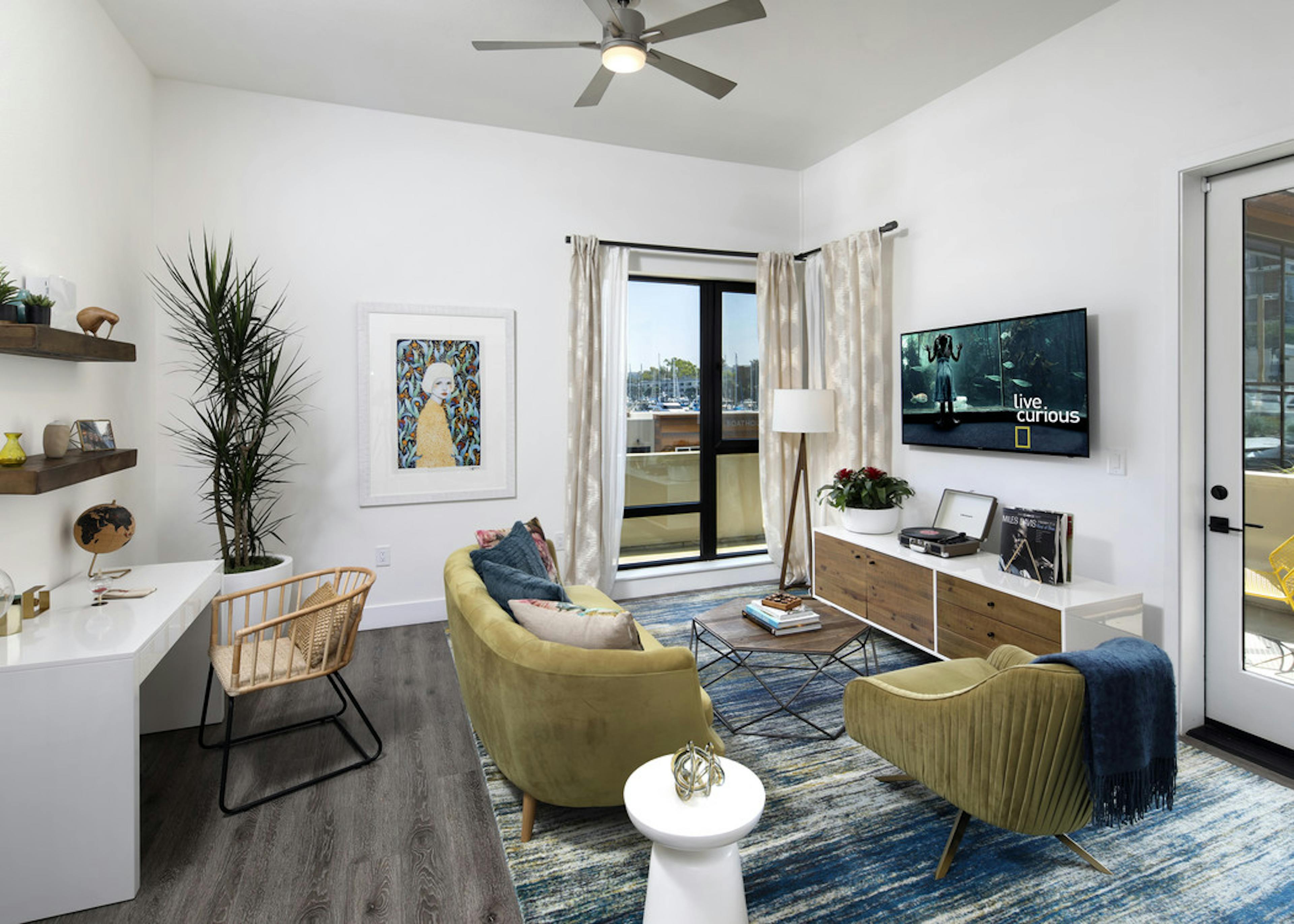 Interior of AMLI Marina Del Rey model living room with couch, coffee table and desk in front of large window facing marina