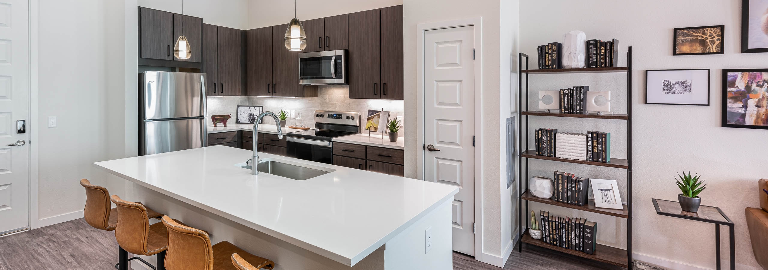 AMLI Art District apartment kitchen with an island and leather bar stools and brown cabinets and stainless appliances