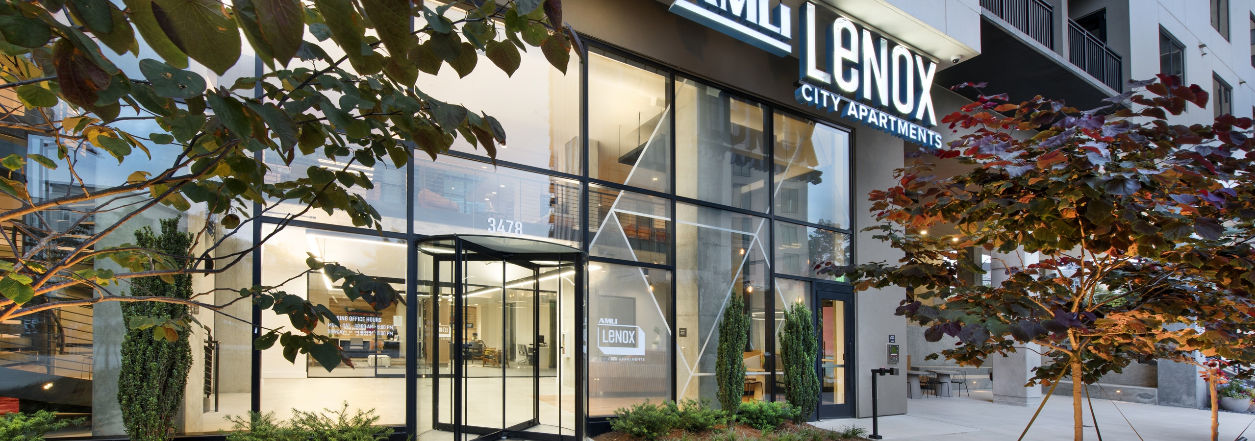 Evening view of AMLI Lenox apartment building entrance with AMLI Lenox sign above two story windows and landscaping