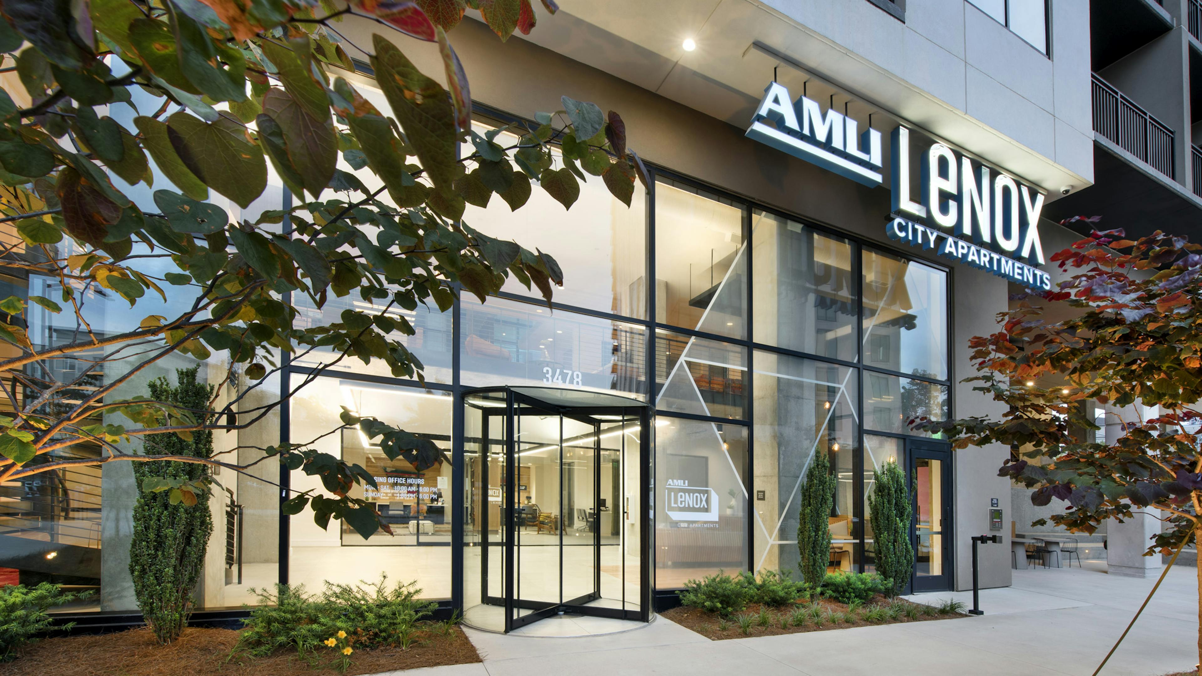 Evening view of AMLI Lenox apartment building entrance with AMLI Lenox sign above two story windows and landscaping