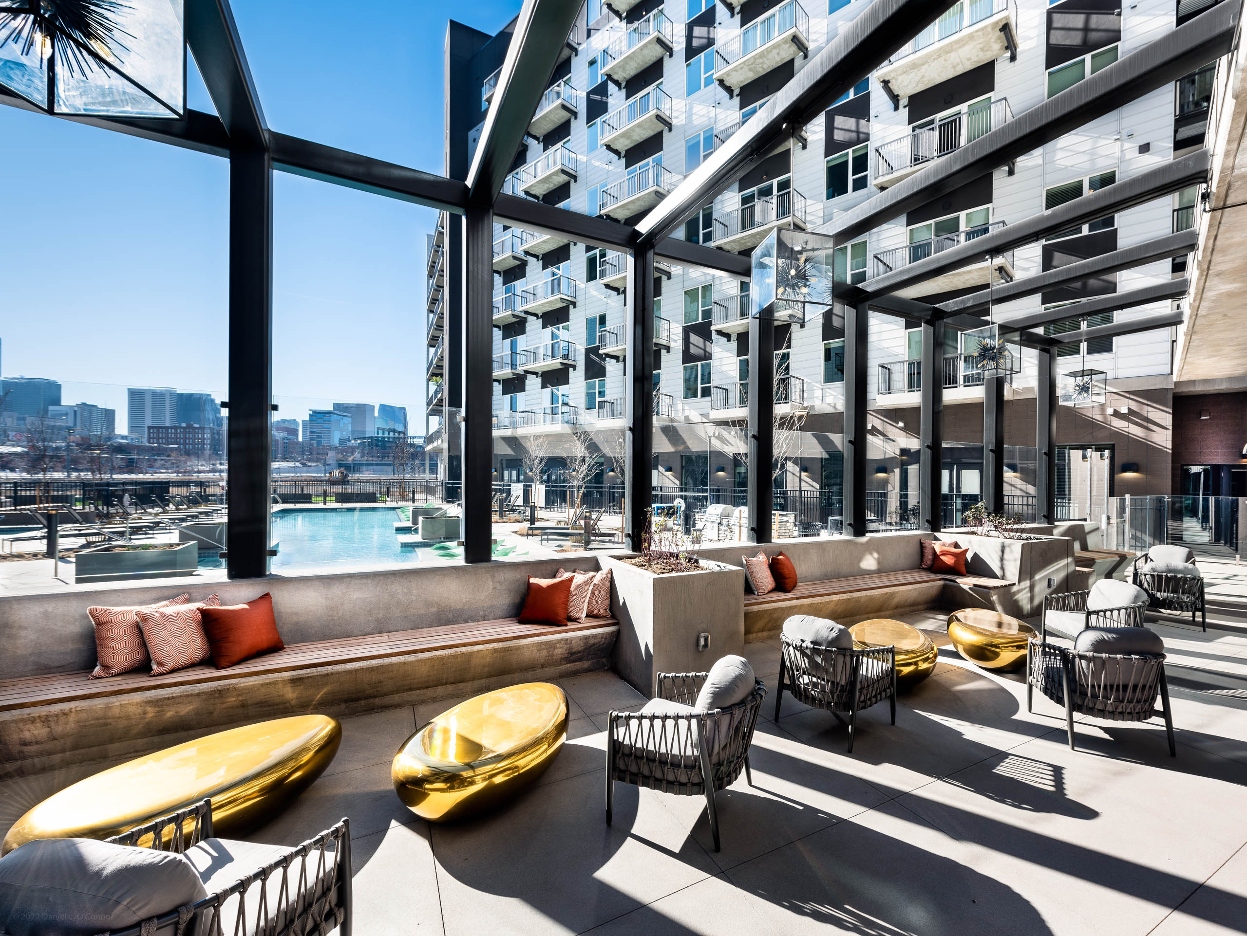 Outdoor lounge at AMLI Art District apartments with chairs and benches and gold coffee tables and a view of the pool