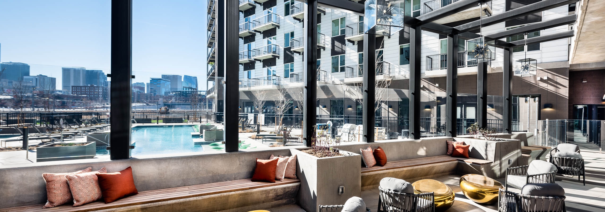 Outdoor lounge at AMLI Art District apartments with chairs and benches and gold coffee tables and a view of the pool
